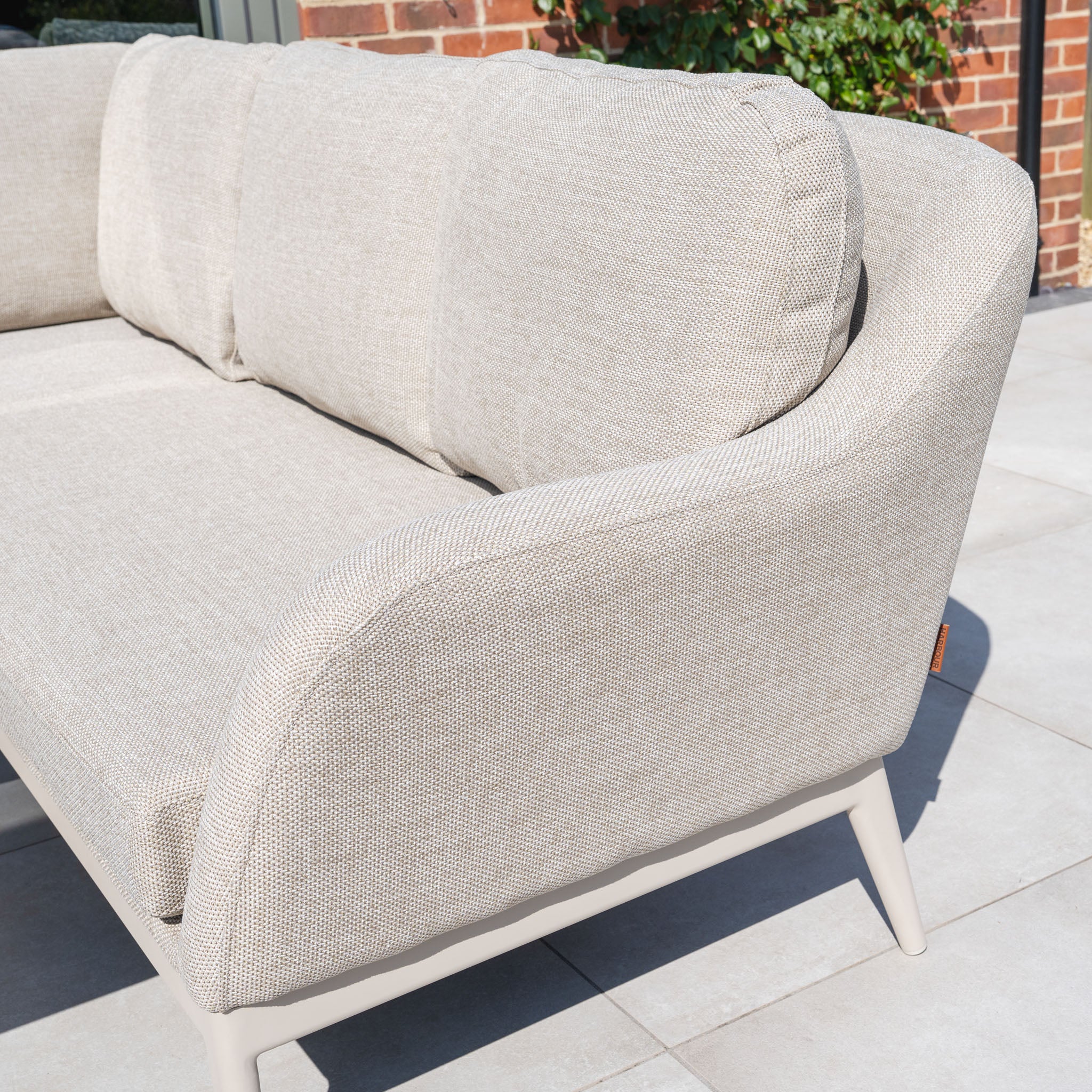 The Luna Outdoor Fabric Rectangular Corner Dining Set with Rising Table in Fawn (Left Hand) features light beige, maintenance-free fabric and curved armrests, perfect for your patio near brick walls and greenery.