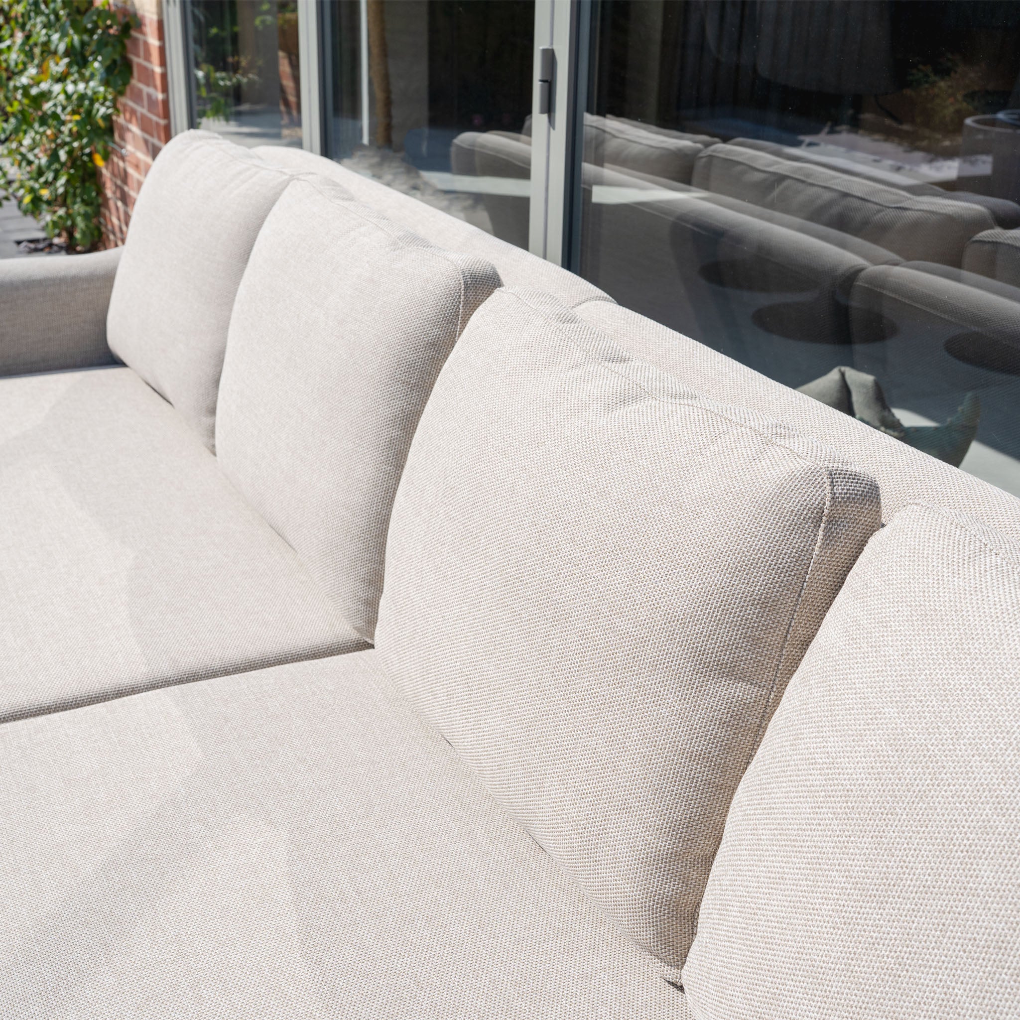 The Luna Outdoor Fabric Rectangular Corner Dining Set with Rising Table in Fawn (Right Hand) features plush, stain-resistant cushions, perfect for sunny spots next to glass sliding doors.