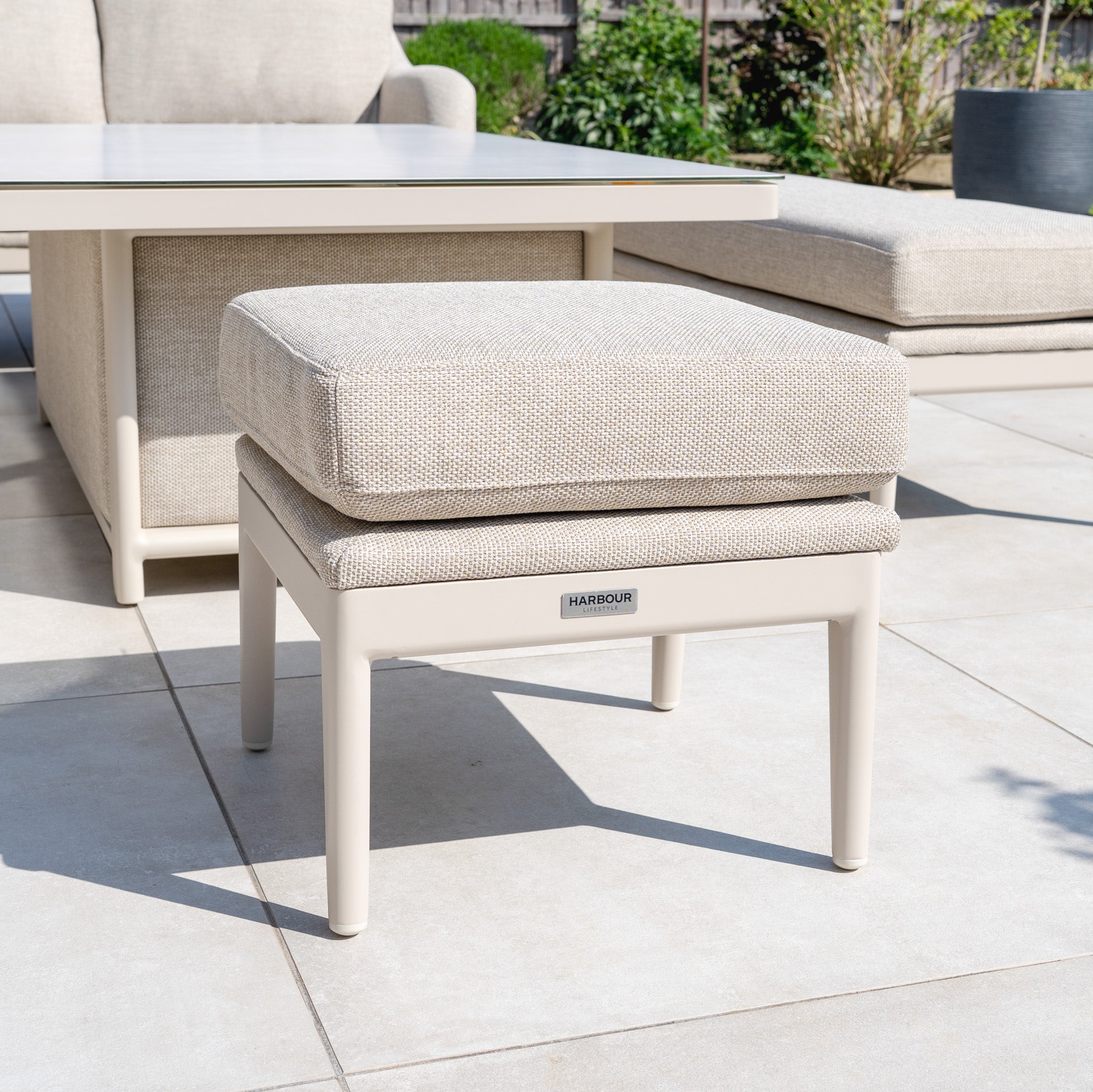 Luna Outdoor Fabric Rectangular Corner Dining Set with Rising Table in Fawn (Left Hand) on tiled patio, surrounded by matching furniture and lush greenery.