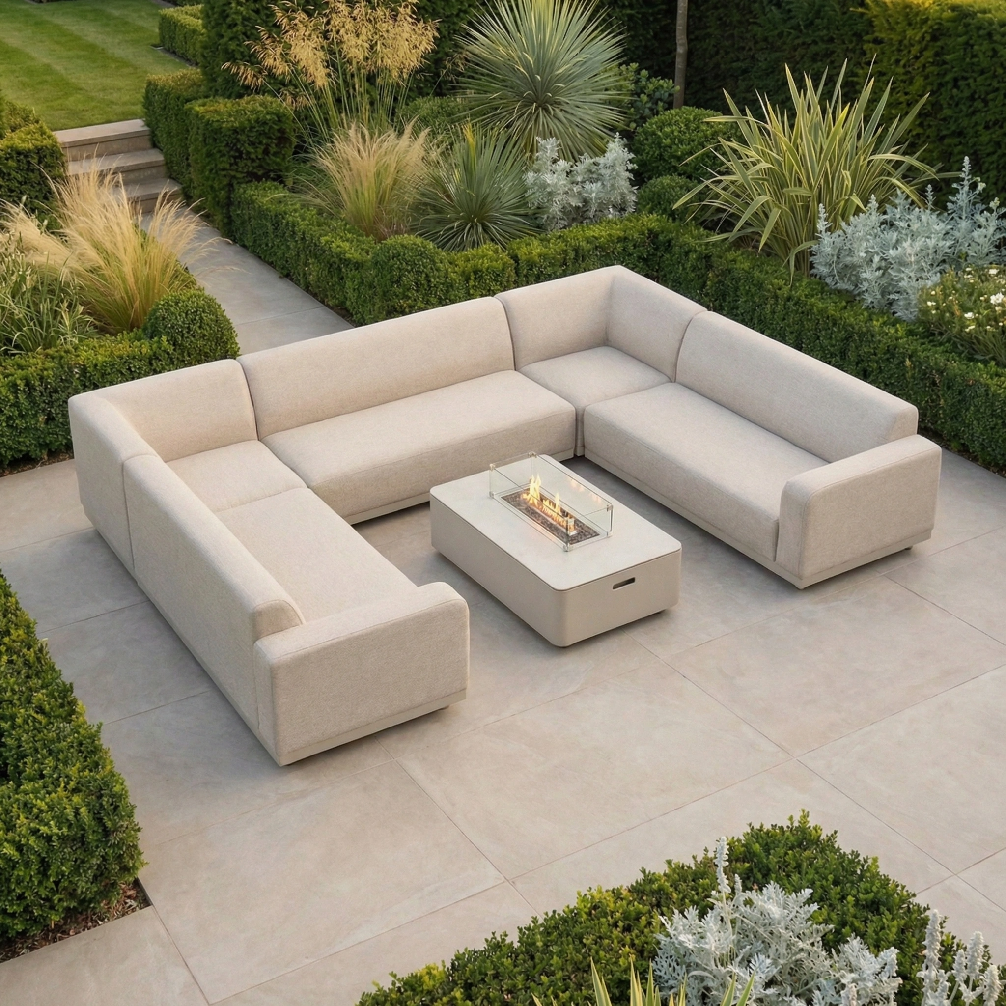 The Luna U-Shape Outdoor Fabric Sofa Set with Firepit Coffee Table in Fawn creates a cozy centerpiece in a beautifully landscaped garden.