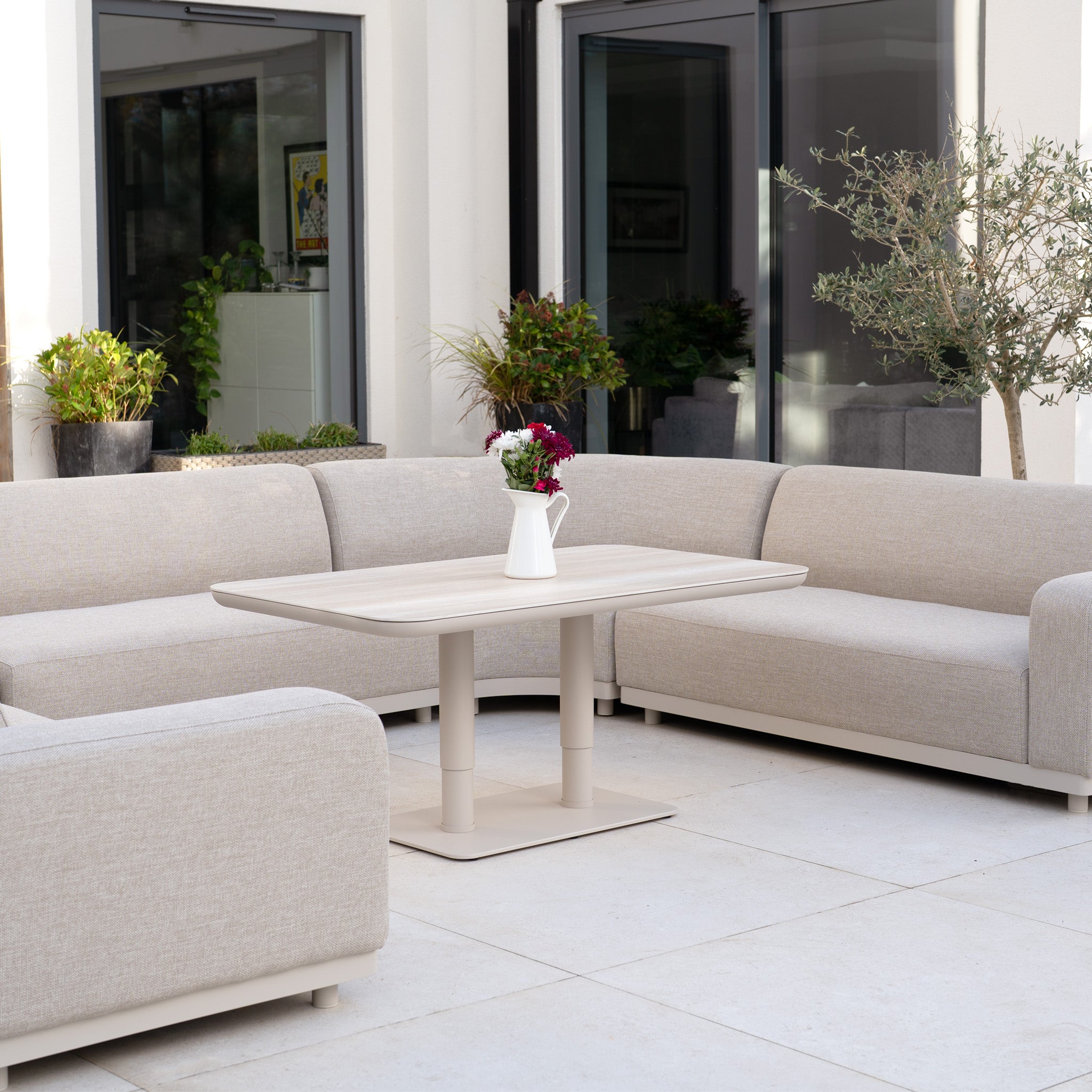 The Luna Outdoor Fabric Curved U-Shape Sofa Set with Altura Rising Table in Fawn creates an inviting patio corner, pairing cozy beige seating with a stylish rising table for elegant all-weather garden gatherings.