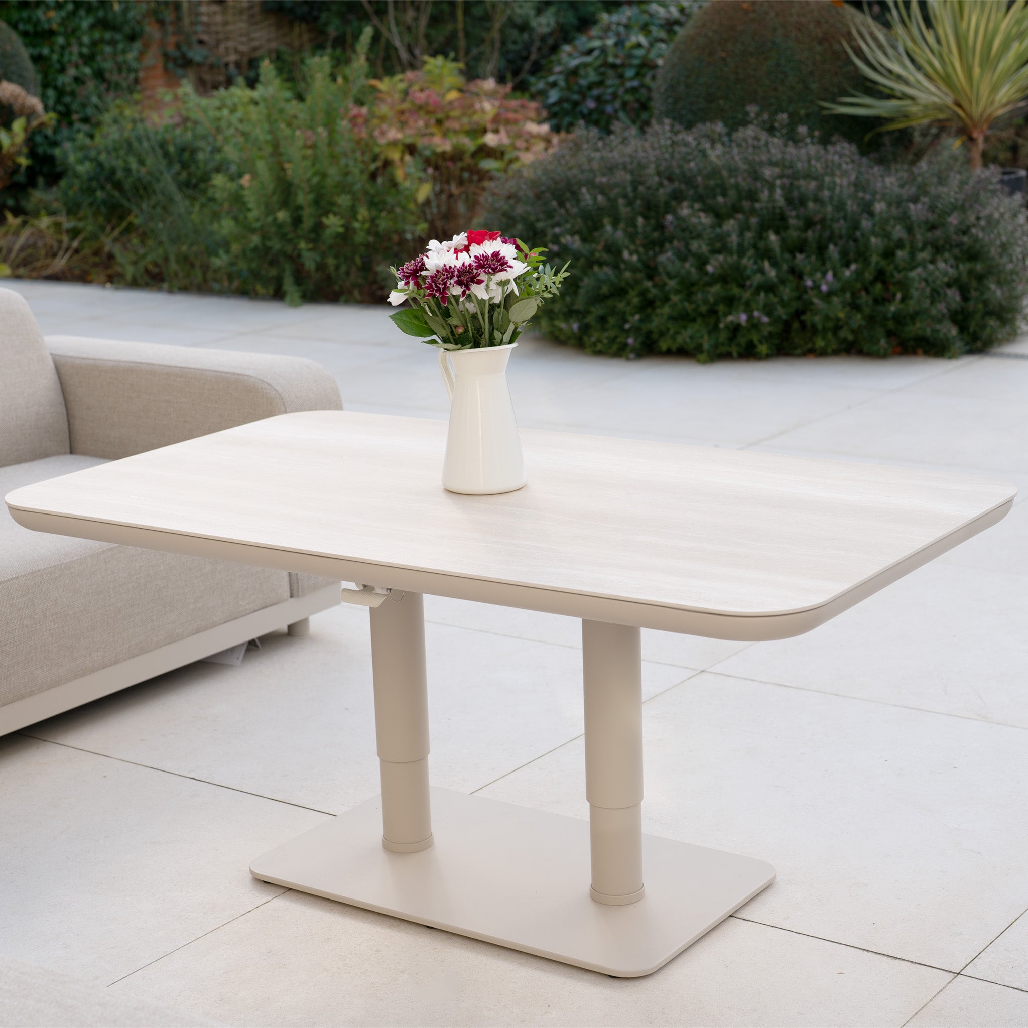 A white vase with flowers sits on a light rectangular table near the Luna Outdoor Fabric Curved U-Shape Sofa Set with Altura Rising Table in Fawn, adding charm to this stylish all-weather garden furniture arrangement.