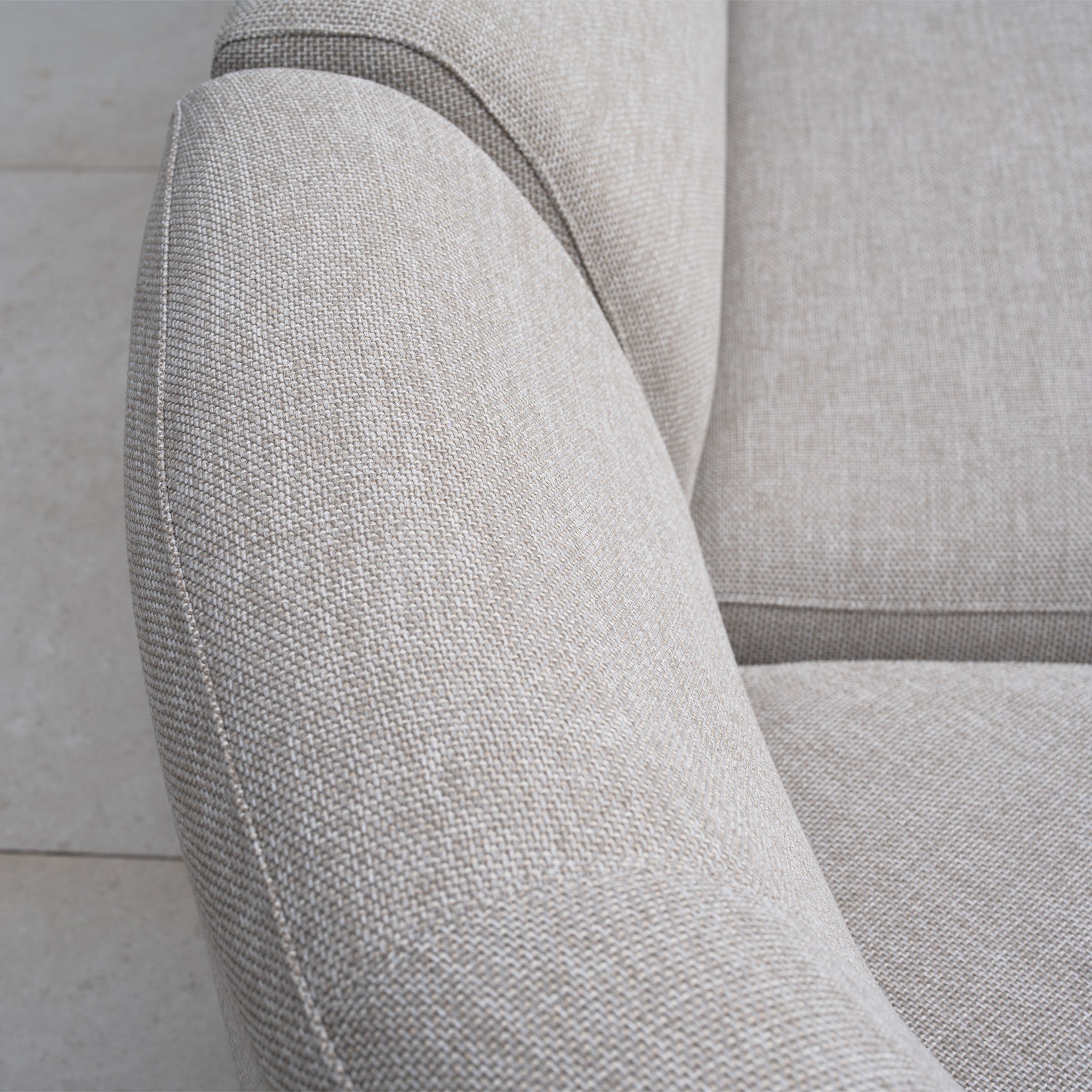 Close-up of a light gray, textured fabric armchair from the Luna Outdoor Fabric Curved U-Shape Sofa Set with Altura Rising Table in Fawn, displayed on a tiled floor—an elegant choice for any all-weather garden furniture ensemble.