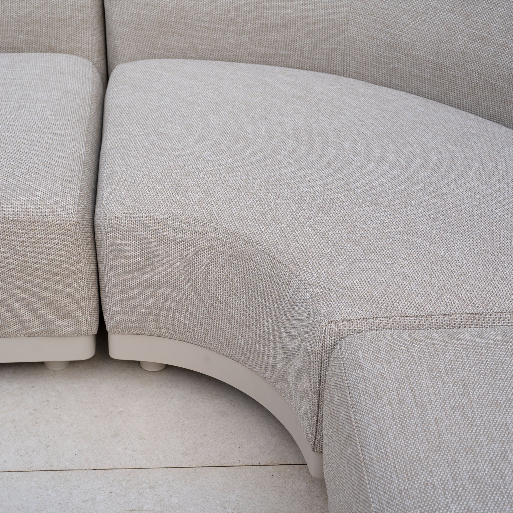 Close-up of the Luna Outdoor Fabric Curved U-Shape Sofa Set with Altura Rising Table in Fawn, featuring textured upholstery on a light tile floor—a refined take on all-weather garden furniture.