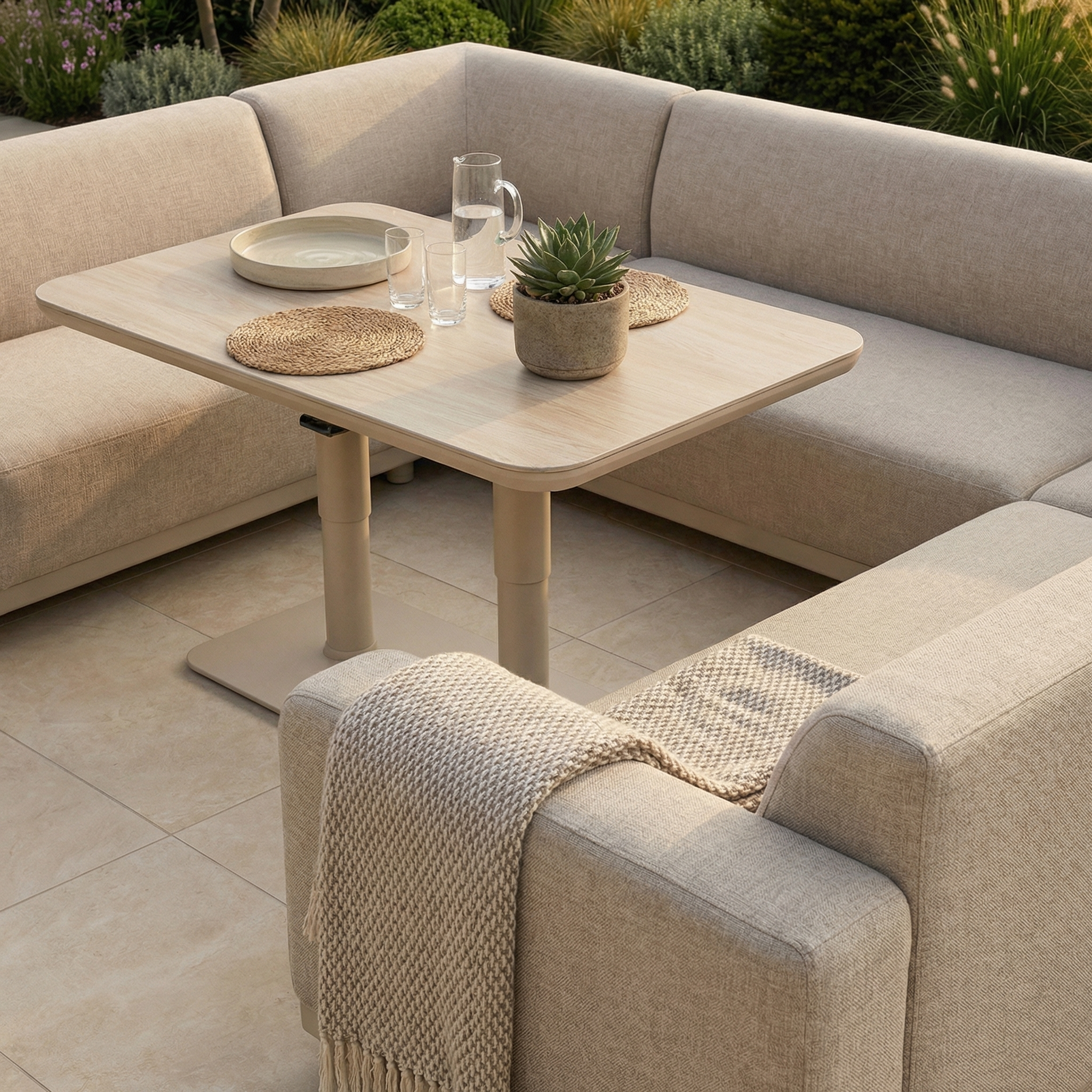The Luna U-Shape Outdoor Fabric Sofa Set with Altura Rising Table in Fawn is arranged with plates, glasses, and a potted succulent on a tiled patio, offering stylish and weather-resistant garden furniture.
