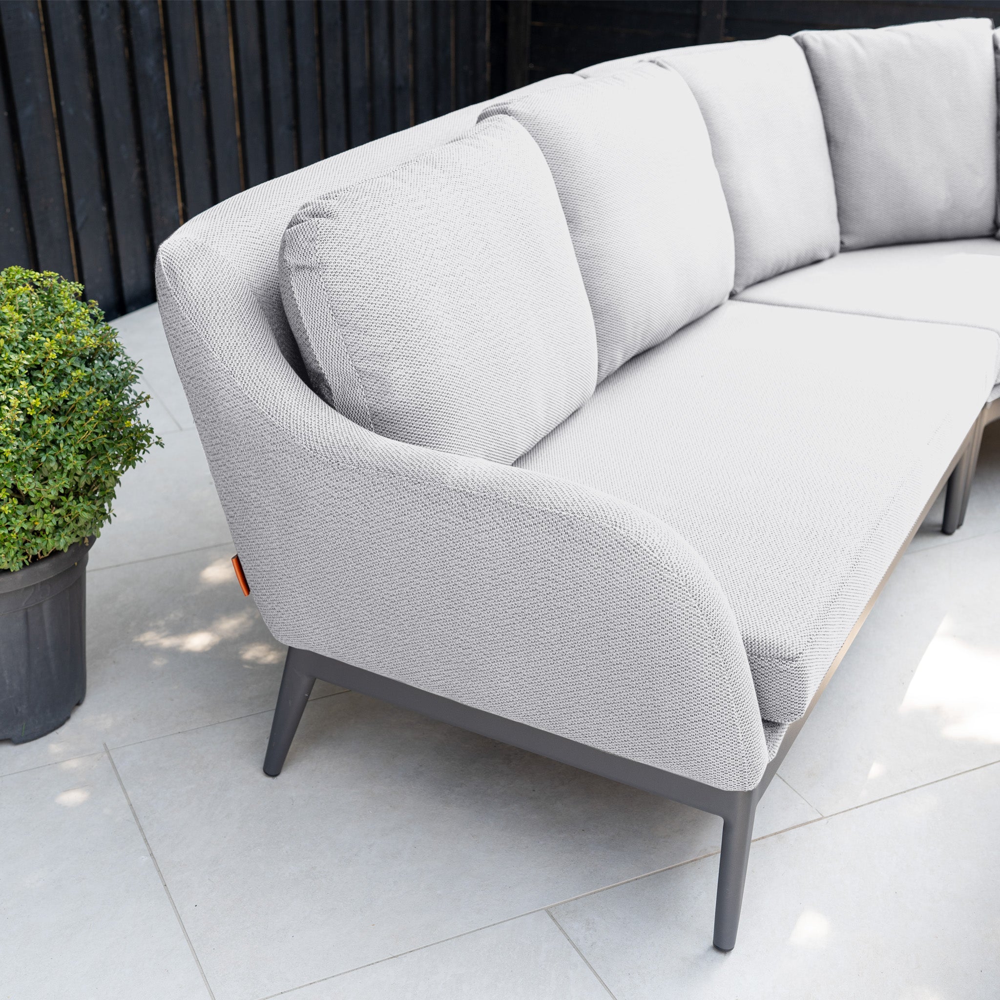 The Luna U-Shape Outdoor Fabric Corner Dining with Rising Table in Oyster Grey features stain-proof cushions and sits on a tiled patio, next to a green potted plant.