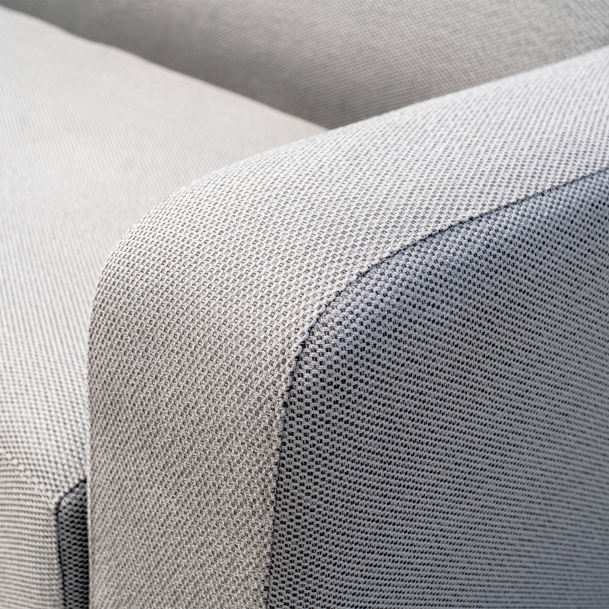Close-up of a Luna U-Shape Outdoor Fabric Curved Corner Group with Round Firepit Coffee Table in Oyster Grey, highlighting the textured armrest and seat on the light grey fabric armchair.