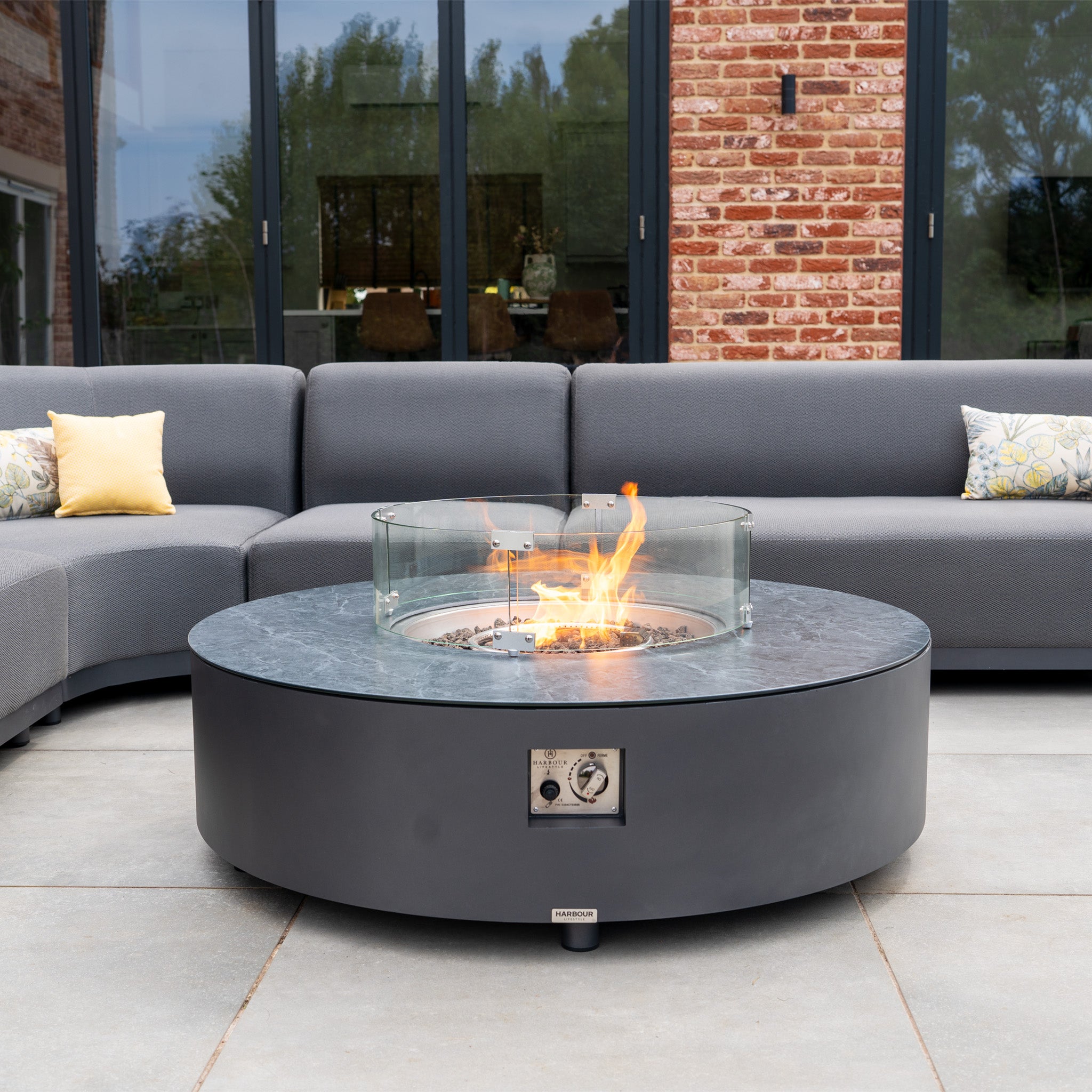 The Luna U-Shape Outdoor Fabric Curved Corner Dining set in grey features a round firepit coffee table with glass wind guard and luxury all-weather corner seating, perfect for a stylish patio.