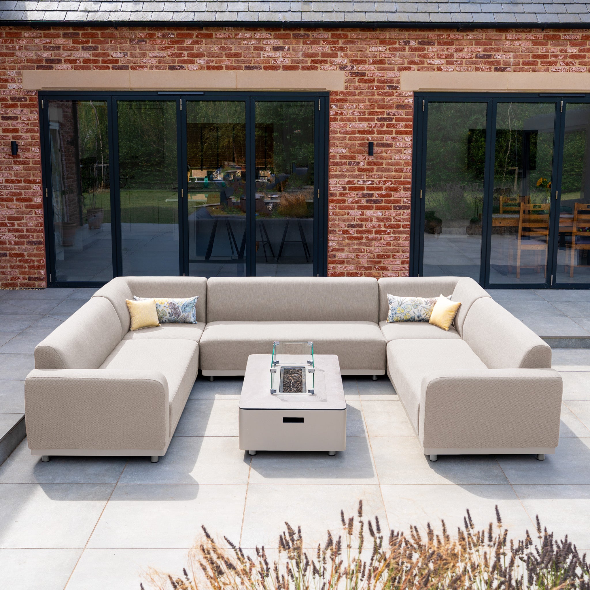 The Luna U-Shape Outdoor Fabric Sofa Set with Firepit Coffee Table in Fawn creates a cozy, weatherproof setting for relaxing outdoors, sitting elegantly in front of glass doors on your patio.