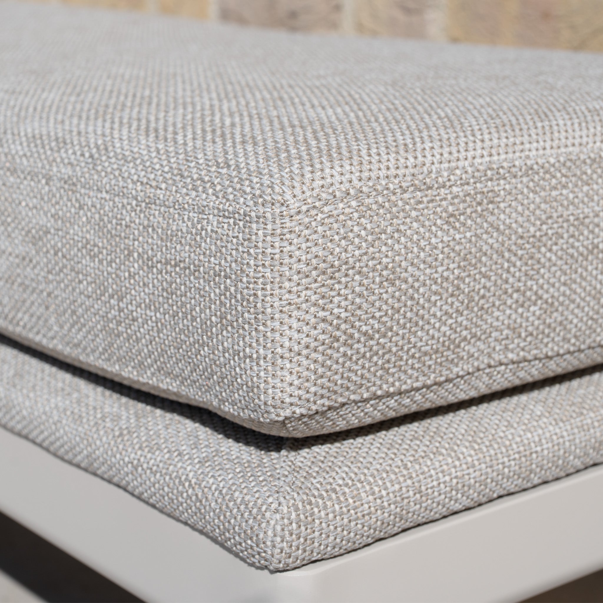 Close-up of two stacked beige textured cushions on the Luna Bench in Fawn, ideal for outdoor seating, with a brick wall in the background.