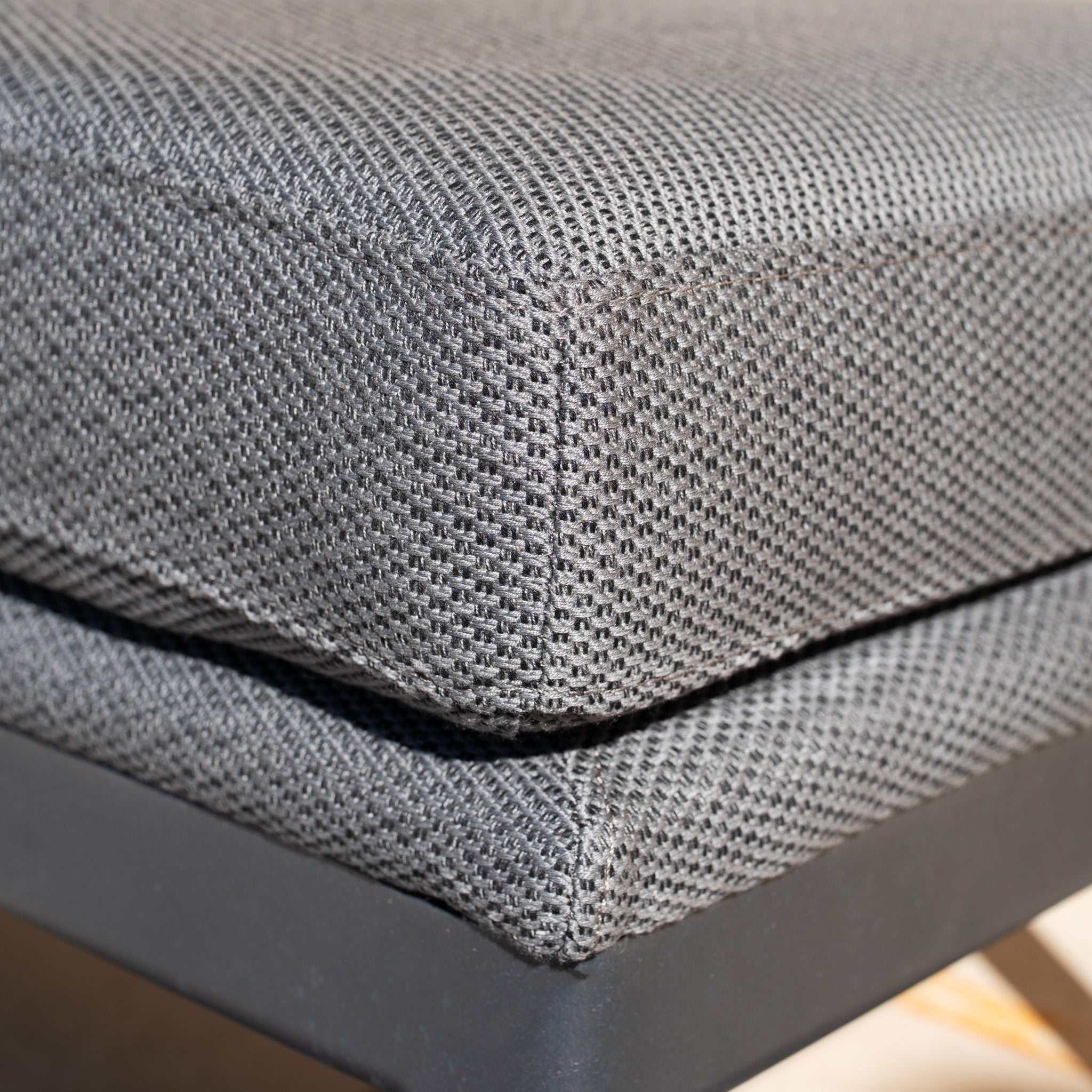 Close-up of a textured grey fabric cushion on the Luna Bench in Grey, an all-weather bench with a sleek black metal frame.
