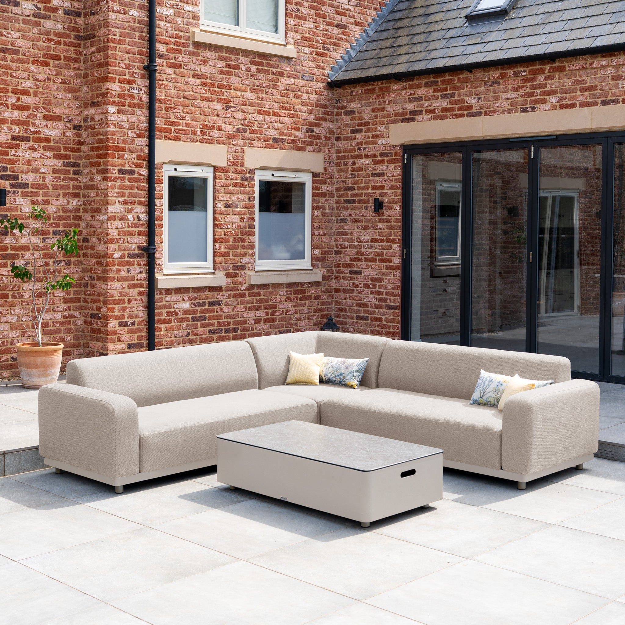 The Luna Outdoor Fabric Corner Sofa Set with Coffee Table in Fawn offers lasting comfort with cushioned seating—a stylish, all-weather sectional perfect for patios by a brick house.
