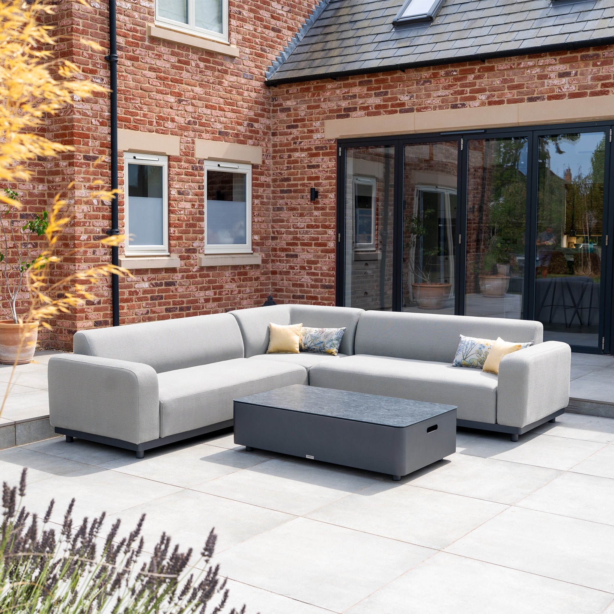 Outdoor patio featuring the Luna Outdoor Fabric Corner Sofa Set with Coffee Table in Oyster Grey and a brick house in the background.