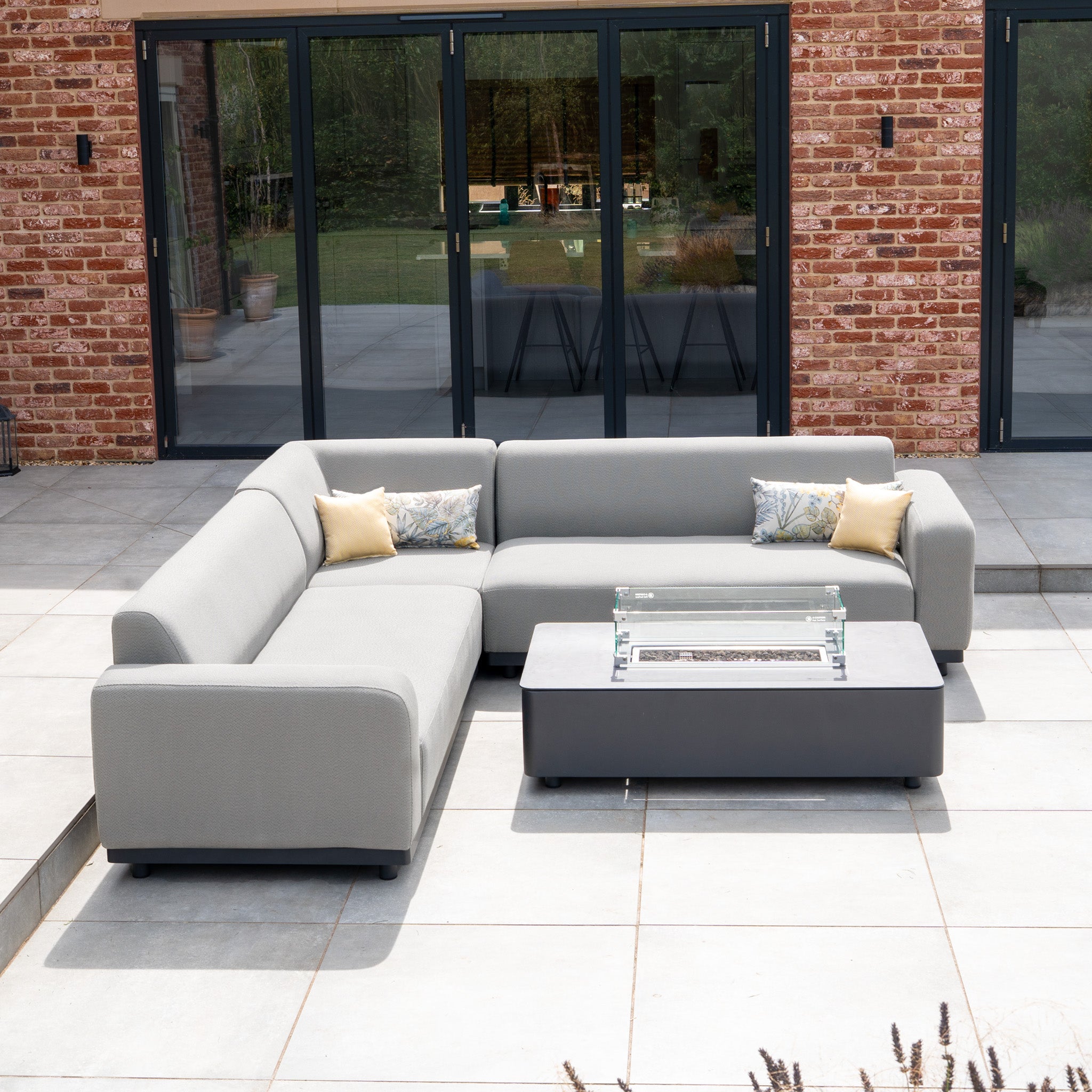 Modern outdoor patio featuring the Luna Outdoor Fabric Corner Sofa Set with Firepit Coffee Table in Oyster Grey, arranged on a tiled terrace.