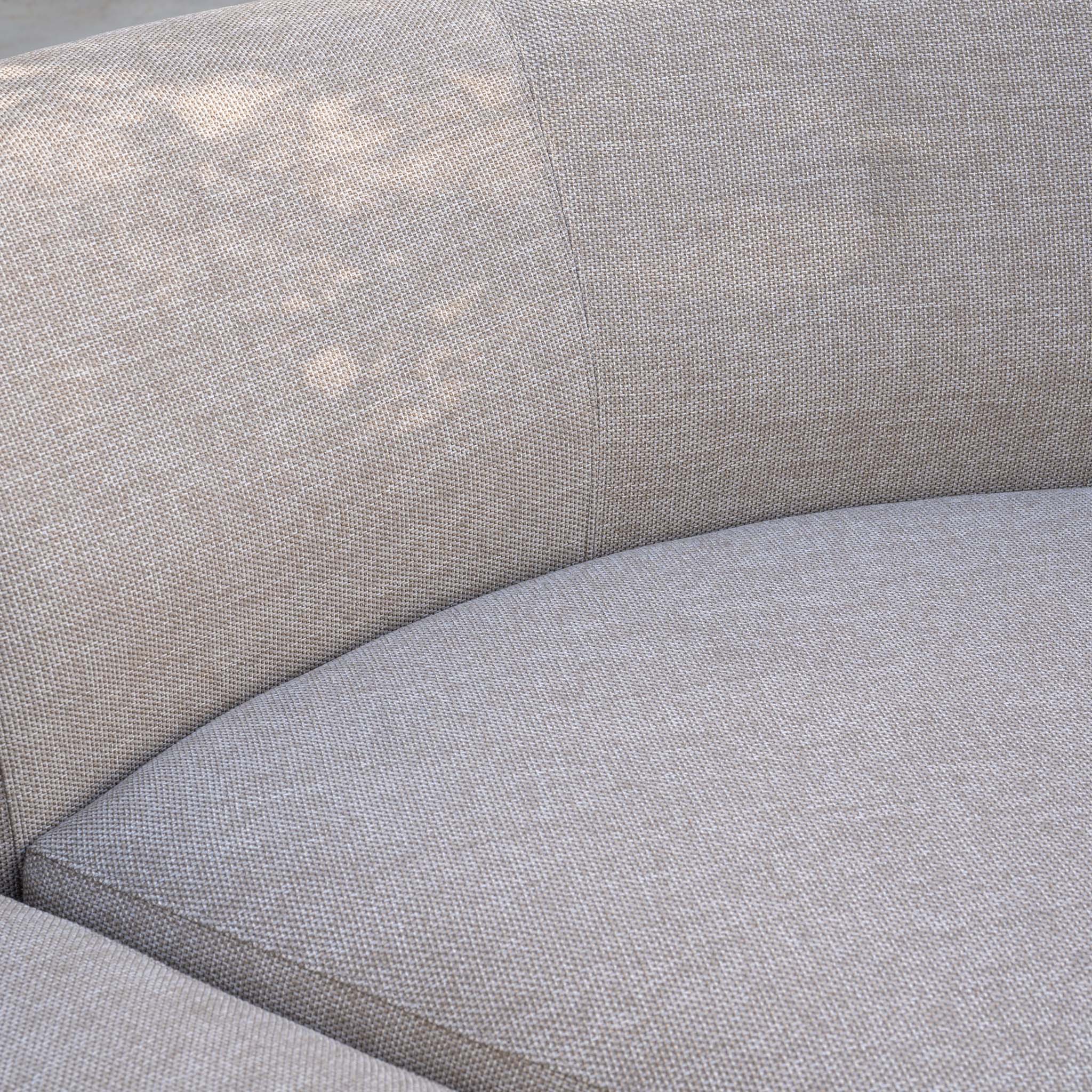 Close-up of the Luna Outdoor Fabric Large Curved Corner Sofa Set with Altura Rising Table in Fawn, highlighting the light beige seat and part of the curved backrest.