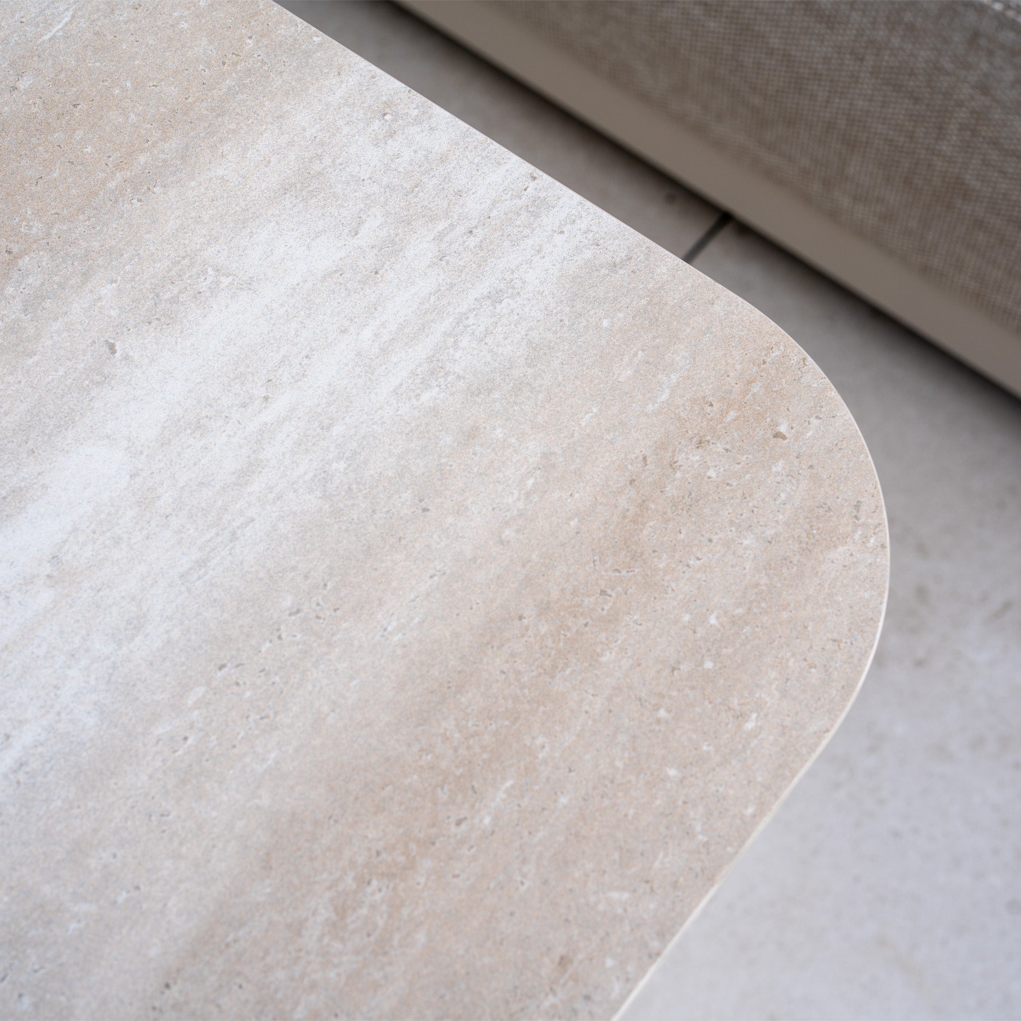 Close-up of the Luna Outdoor Fabric Large Curved Corner Sofa Set with Altura Rising Table in Fawn, showing the smooth tabletop and soft sofa textures—refined details ideal for stylish all-weather garden furniture.