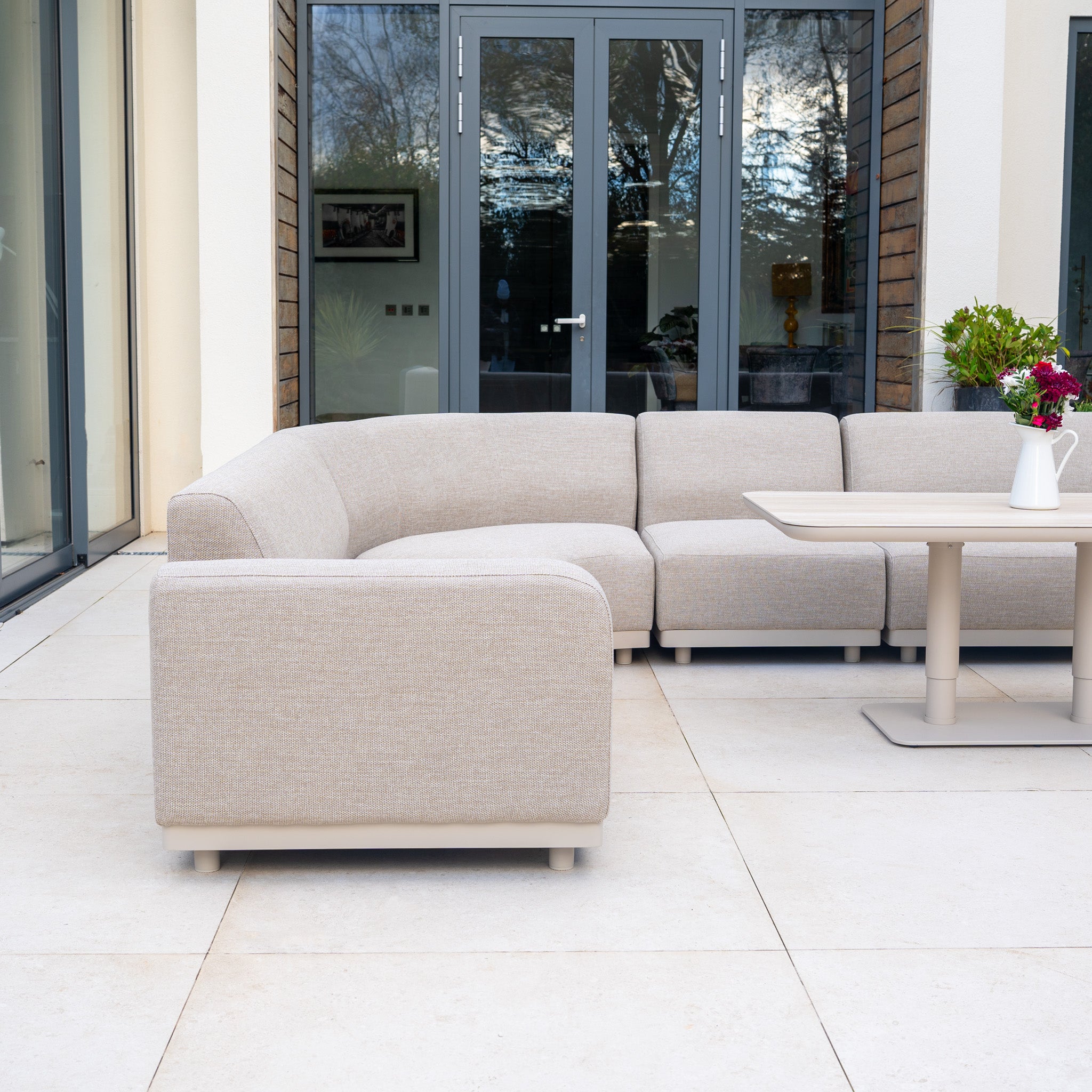 The Luna Outdoor Fabric Large Curved Corner Sofa Set with Altura Rising Table in Fawn offers quick-dry cushions and a stylish look, perfect for modern patios outside glass doors.