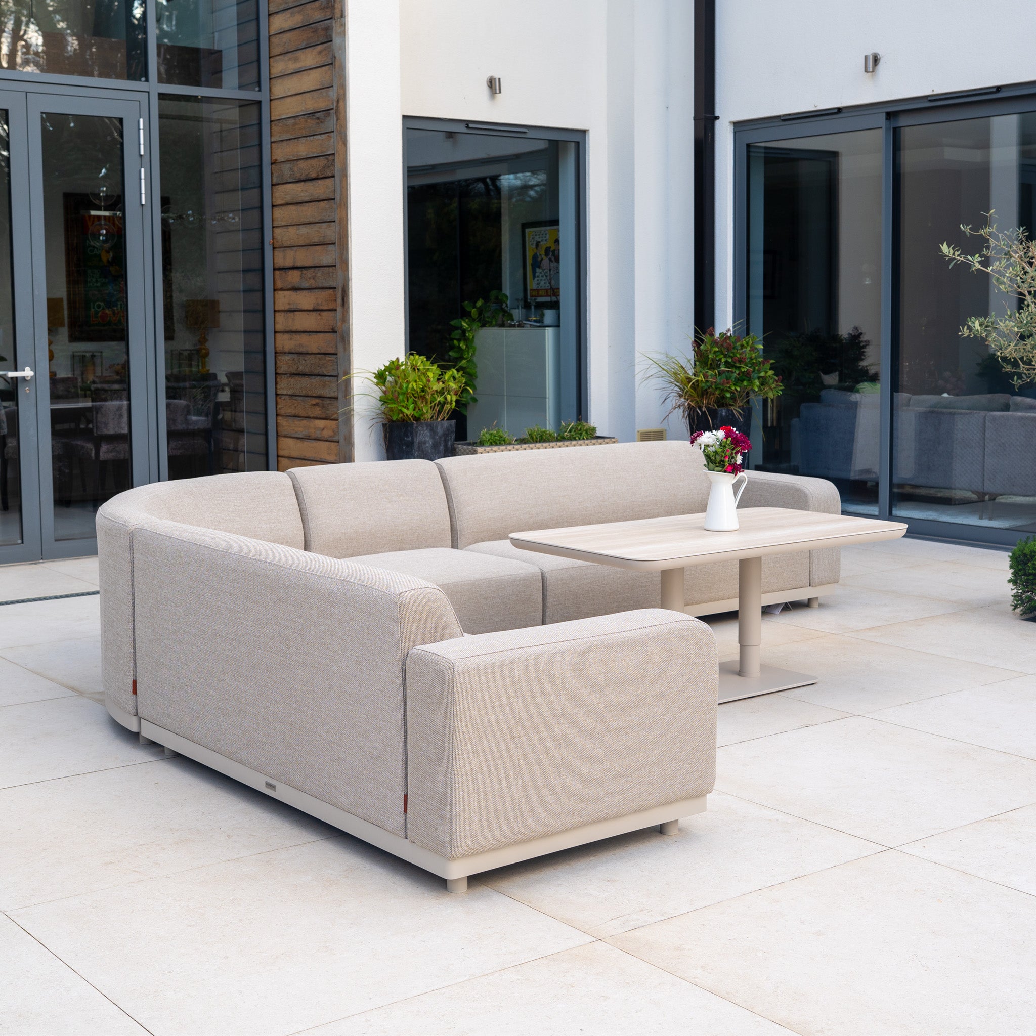 The Luna Outdoor Fabric Large Curved Corner Sofa Set with Altura Rising Table in Fawn offers quick-dry cushions and all-weather comfort, perfect for relaxing in style on your modern patio or garden.