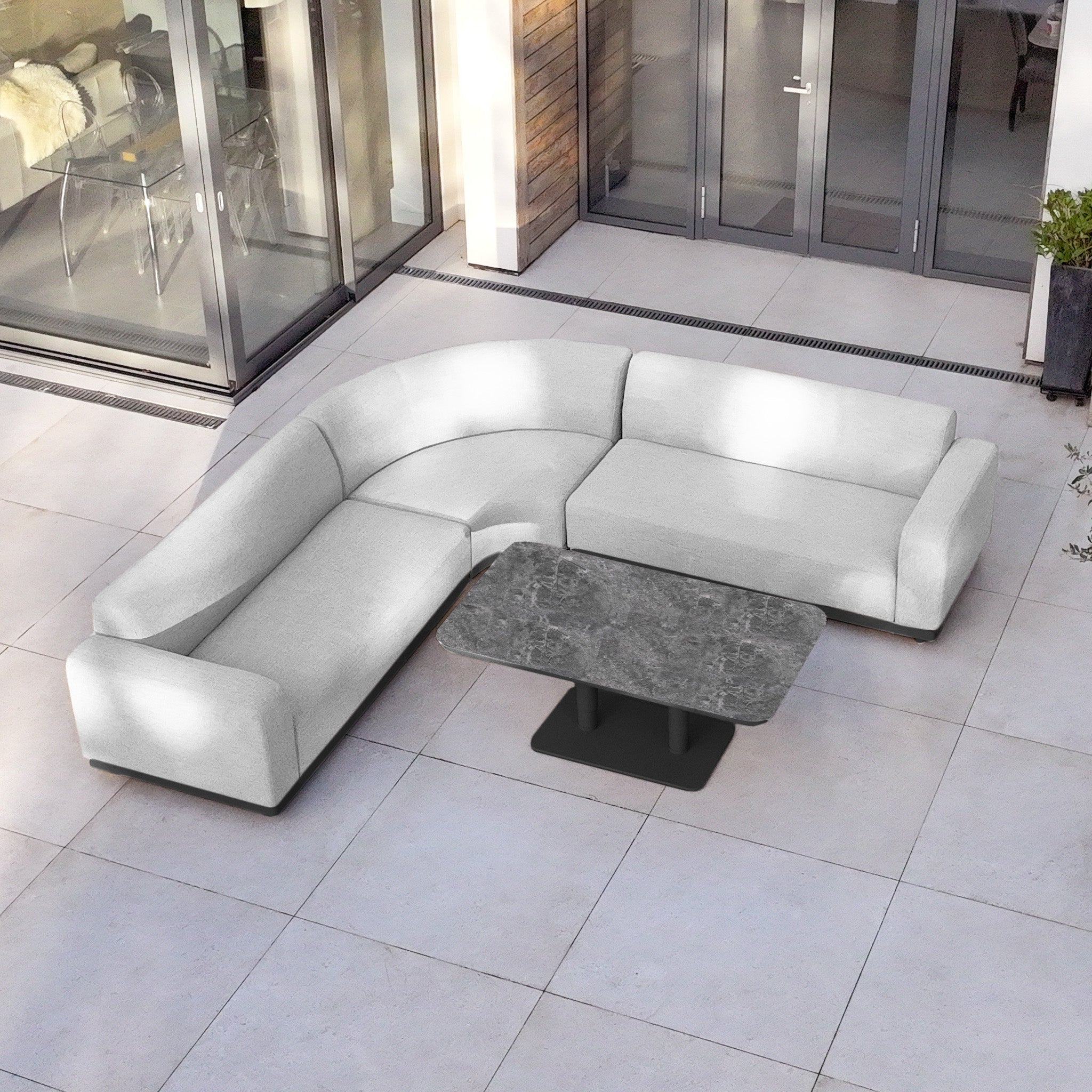 Luna Outdoor Fabric Curved Corner Sofa Set with Altura Rising Table in Oyster Grey on a light tiled patio—an elegant, all-weather garden furniture ensemble.