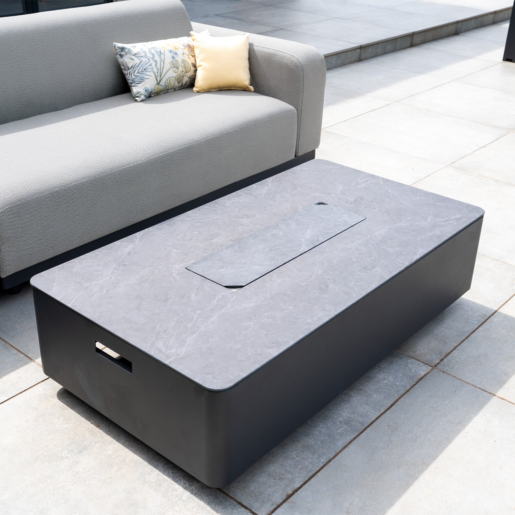The Luna Outdoor Fabric Large Corner Group Set with Firepit Coffee Table in Oyster Grey features a gray marble-top firepit table and modern cushioned sofa, perfect for relaxing on a tiled patio.