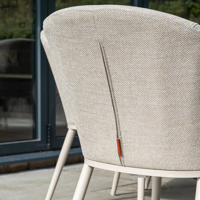 The Luna 8 Seat Outdoor Fabric Extending Ceramic Dining Set in Fawn features textured, stain-proof fabric seen from the back, arranged outdoors near glass doors.