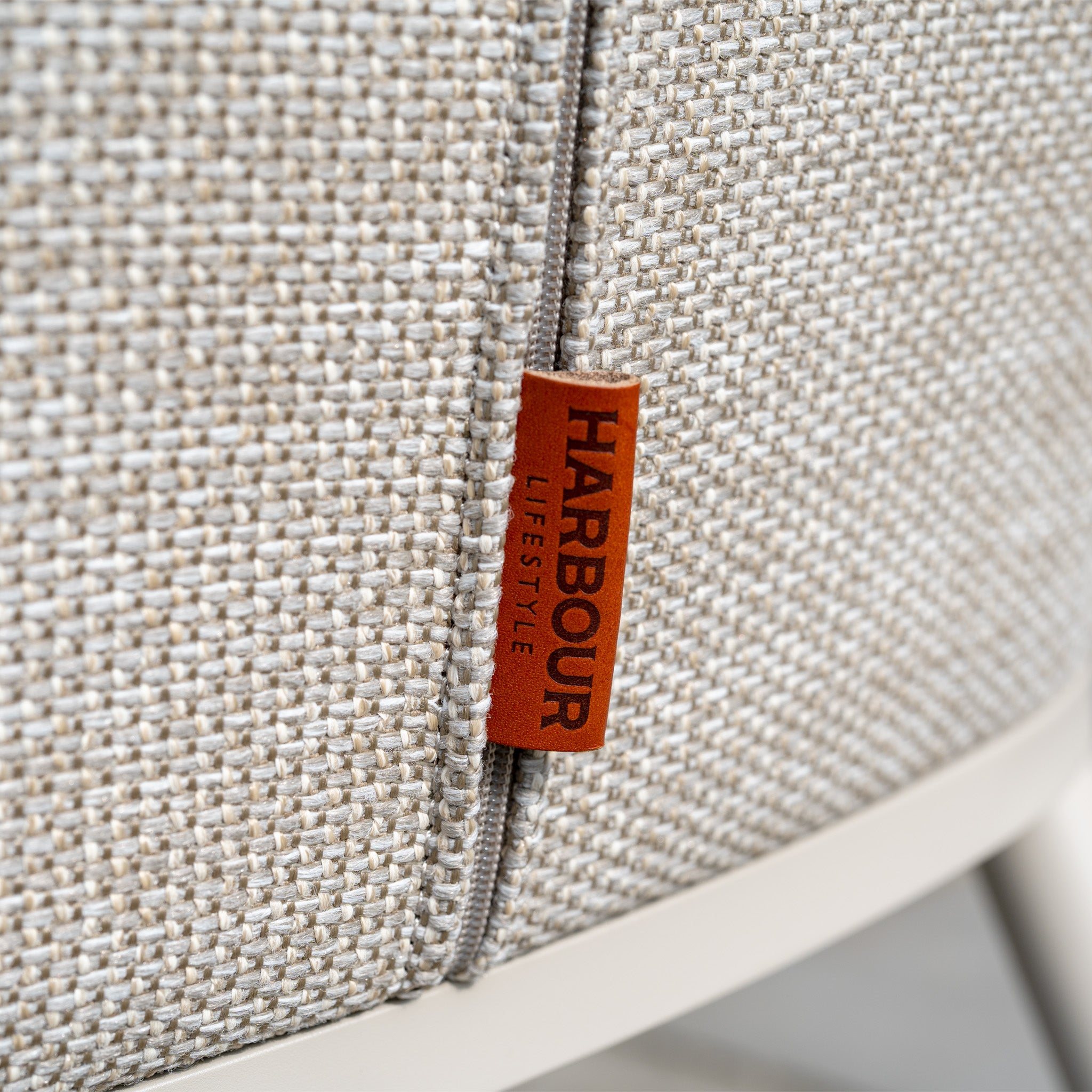 Close-up of a beige textured Luna 6 Seat Outdoor Fabric Oval Ceramic Dining Set in Fawn with a brown "Harbour Lifestyle" label attached.