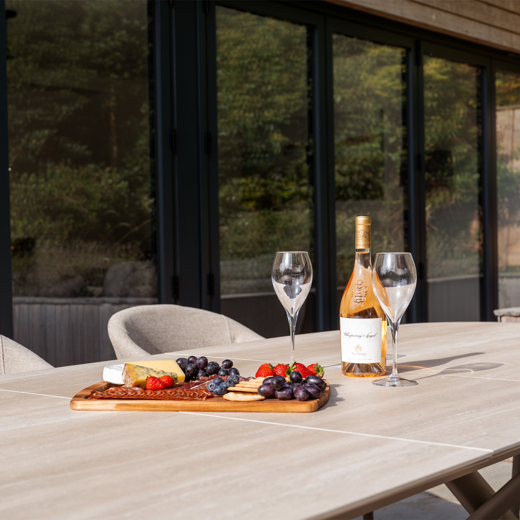 A modern outdoor table set with wine, glasses, cheese, crackers, and fruit showcases the Luna 8 Seat Outdoor Fabric Oval Dining Set with Albatross Extending Table in Fawn, featuring UV resistant cushions for comfort and style.