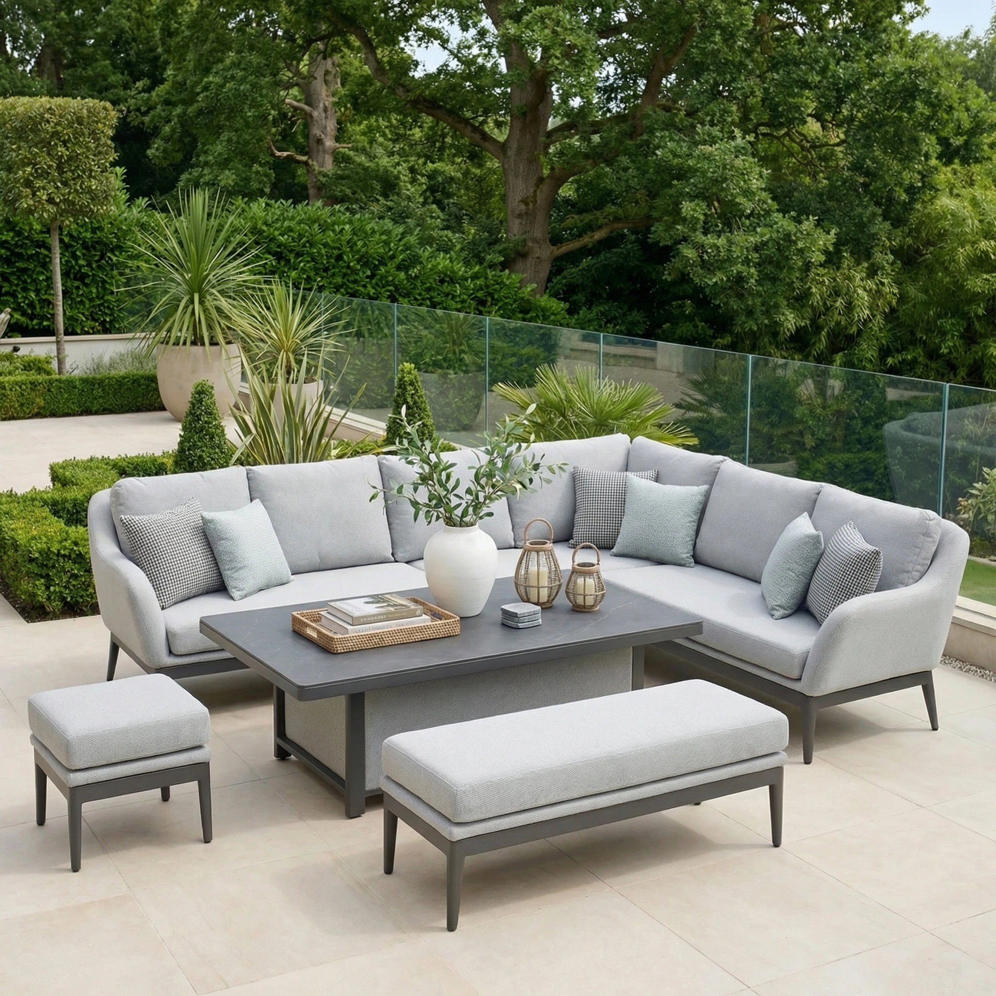 The Luna Outdoor Fabric Rectangular Corner Dining Set with Rising Table in Oyster Grey (Right Hand) features plush cushions, benches, and a rising table, perfect for a tiled terrace amidst lush greenery.