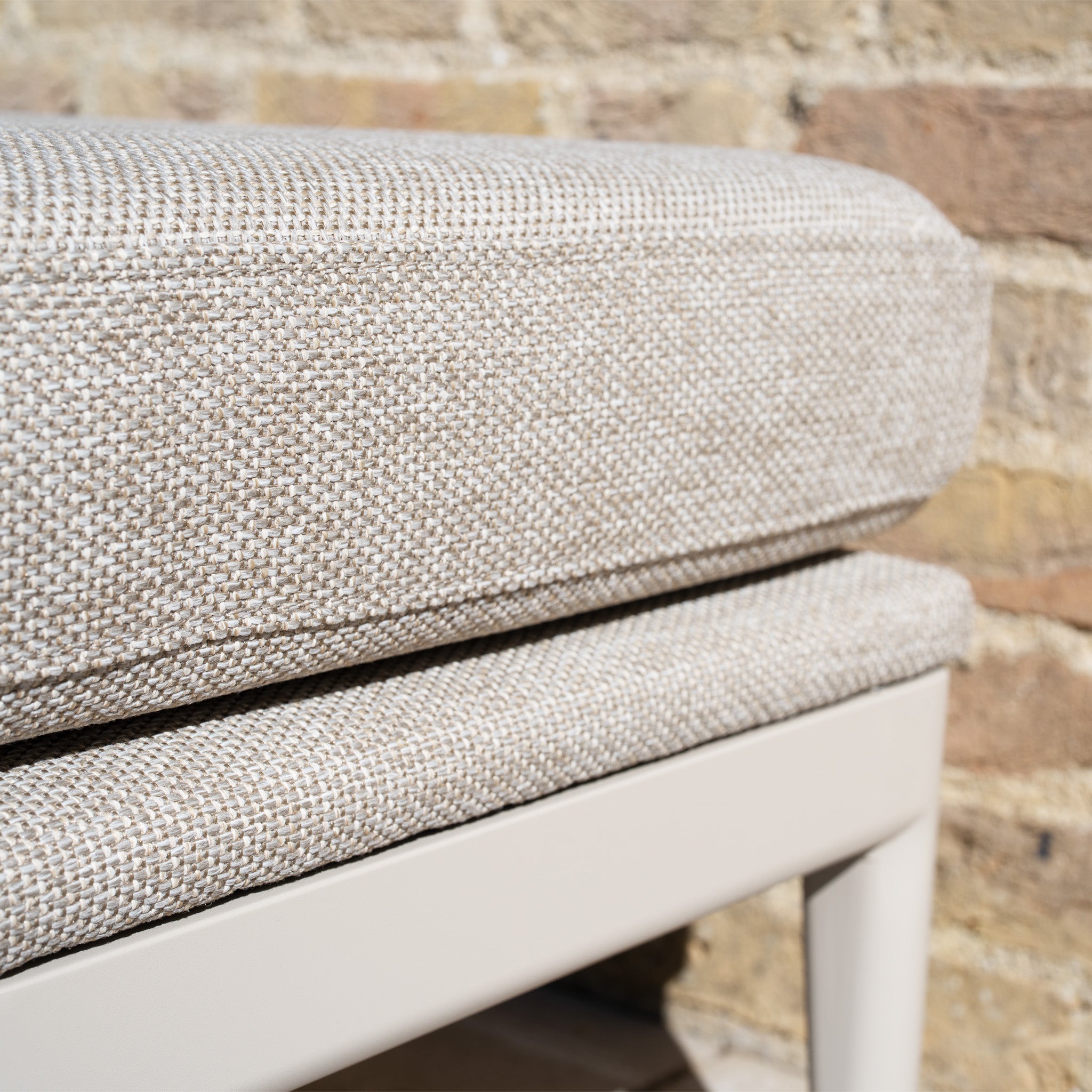 Close-up of a beige woven cushion with quick-dry foam on a light bench, set against a brick wall—perfect for pairing with the Luna Stool in Fawn, our all-weather outdoor stool.