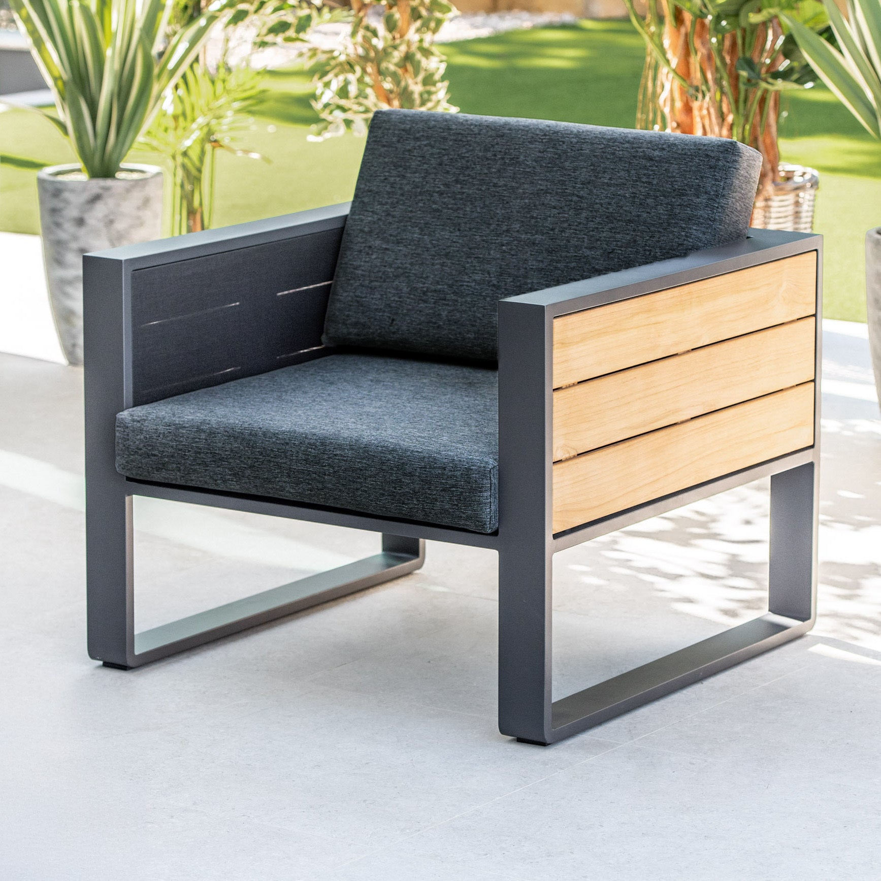 Modern outdoor furniture: the Manhattan Armchair with Teak Gas Lift Arm in Charcoal features a sleek metal frame, wooden side panels, and Olefin seat cushions—perfect for your patio.