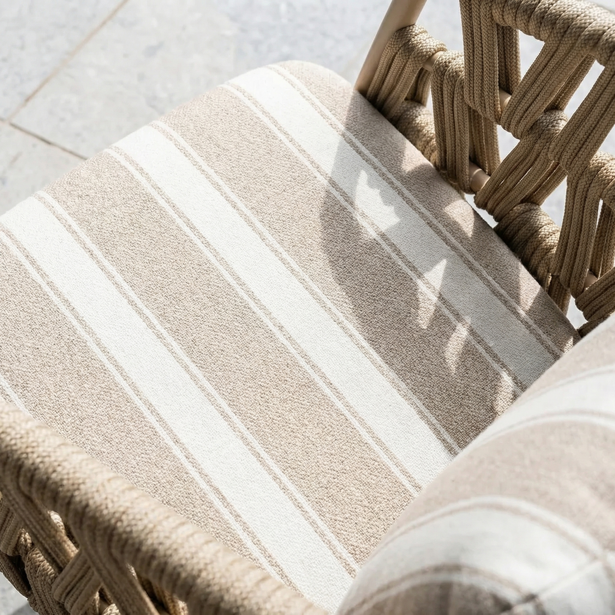 The Madeira 6 Seat Curved Rectangular Dining Set in Striped Latte features a woven chair with a beige and white striped cushion, bathed in sunlight, beside a powder-coated aluminium dining table.