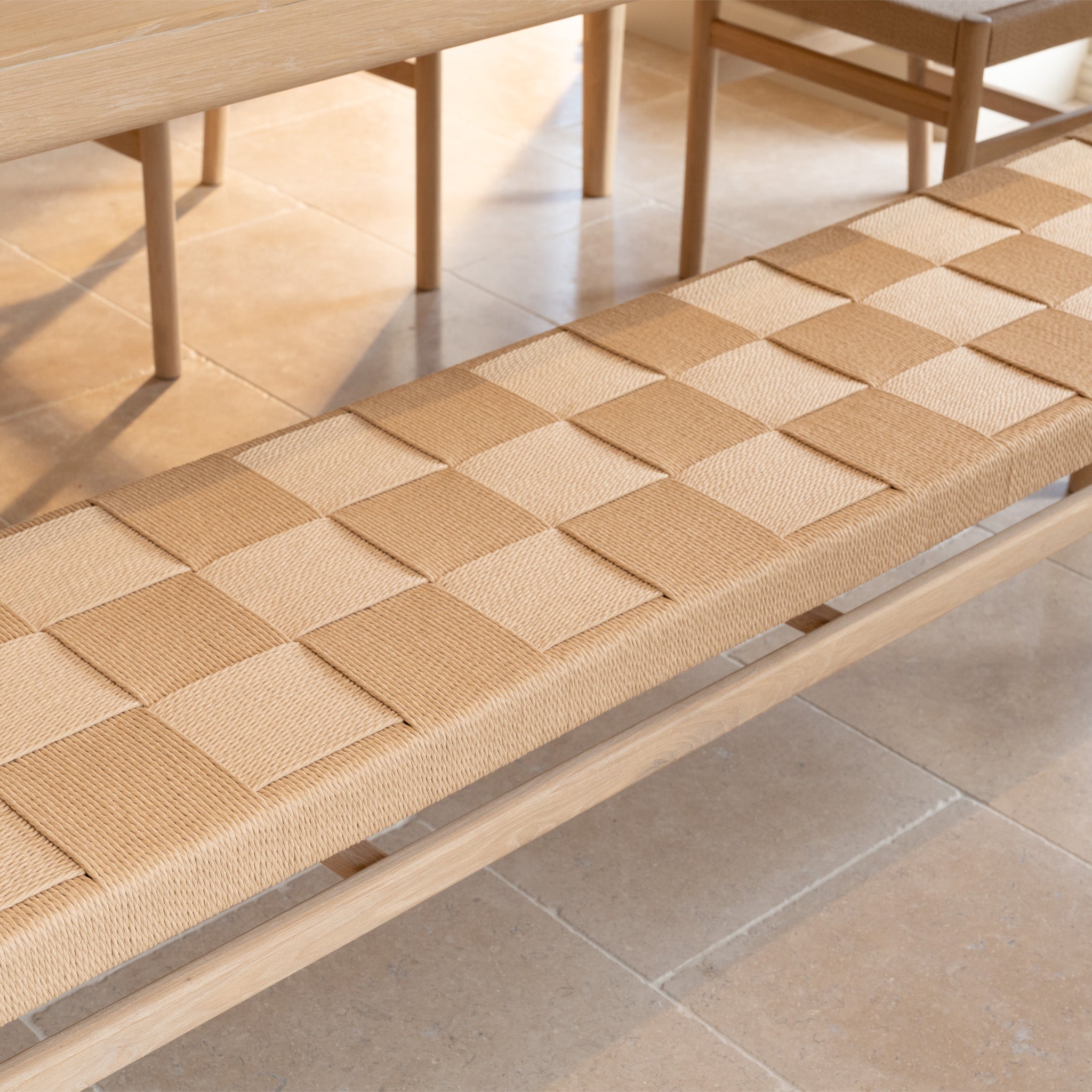 Woven bench with a checkered pattern on a tiled floor, next to the Marlow 8 Seat Dining Set with Woven Bench in Light Oak.