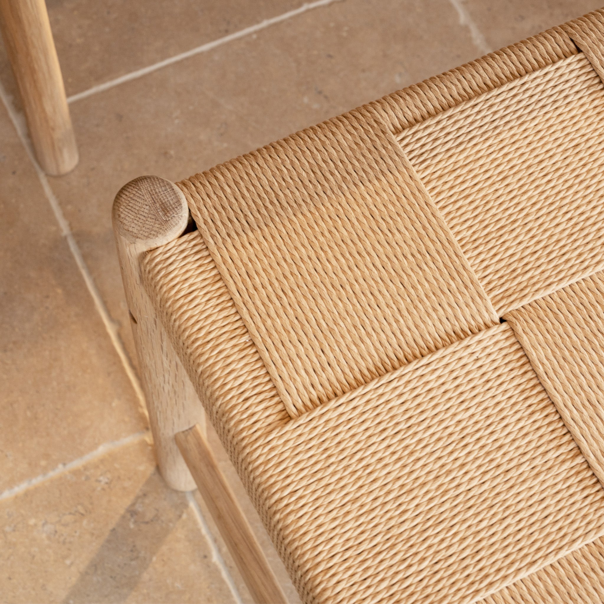 Close-up of the Marlow Woven Dining Bench in Light Oak, featuring a natural fiber seat, shown on a tiled floor.