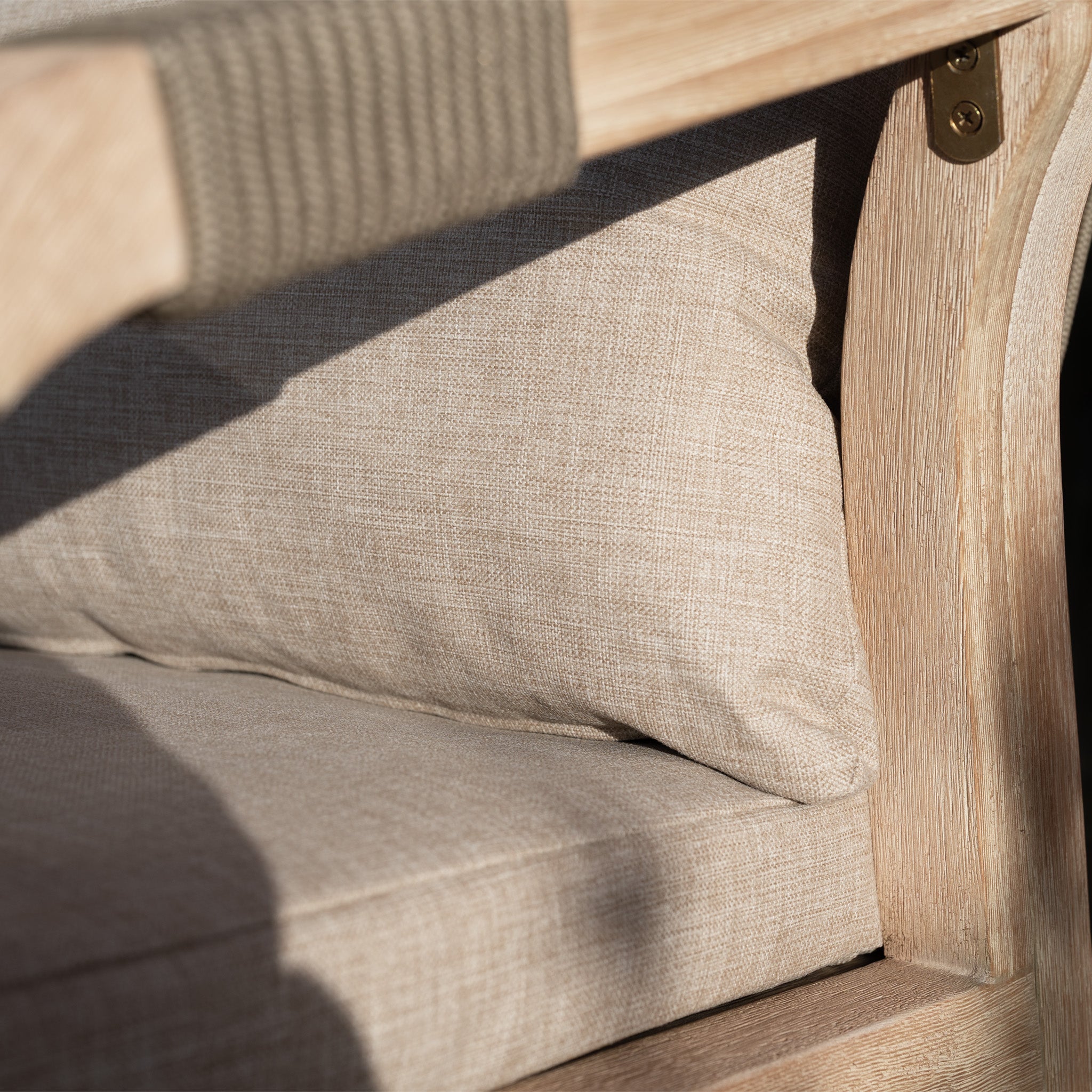 Close-up of a beige cushion and seat on a wooden chair with sunlight casting shadows, highlighting the rope-weave backrest from the Quay Corner Sofa Dining Set in Mocha.