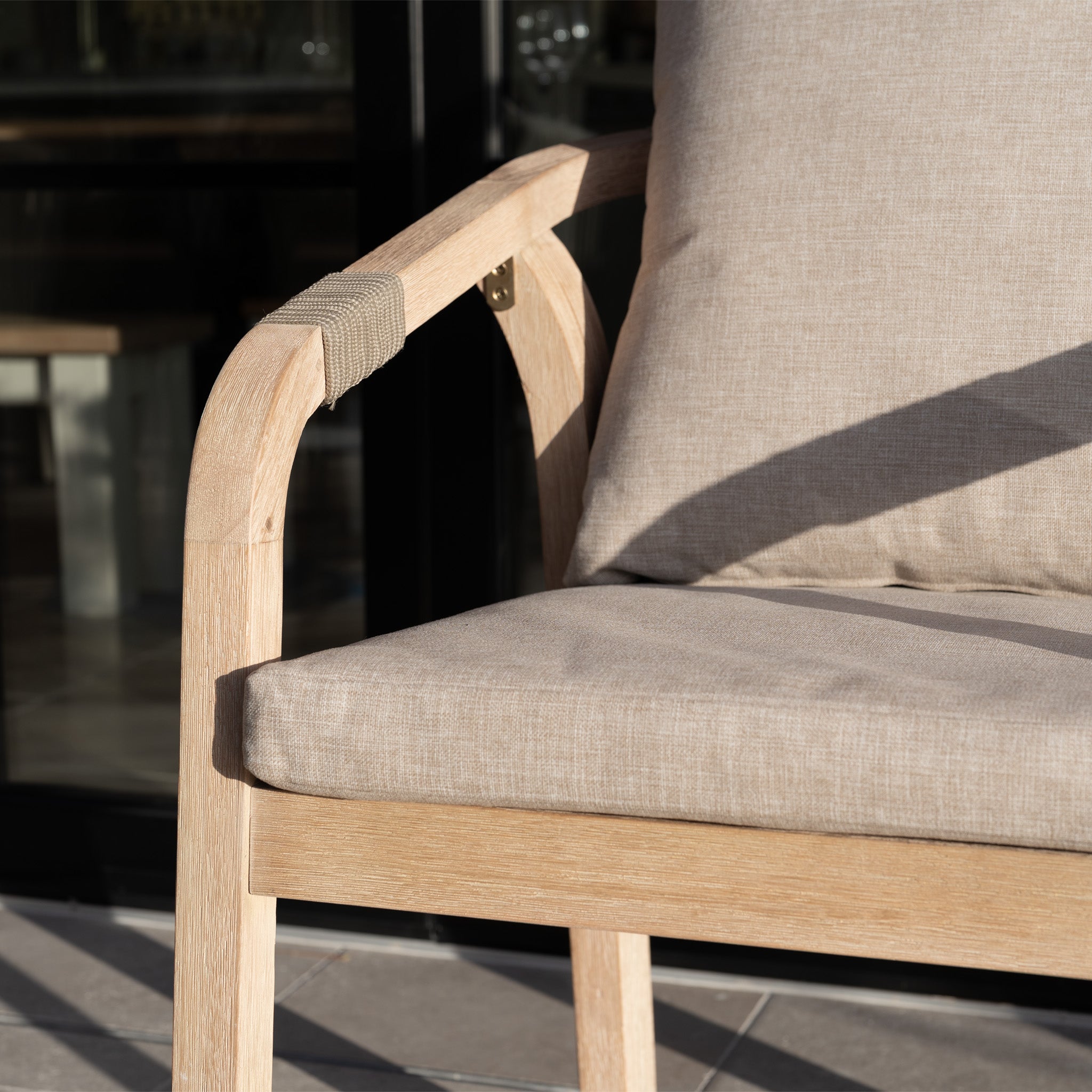 Close-up of the Quay 4 Seat Round Dining Set in Mocha, featuring a wooden chair with beige cushions, shown outdoors in sunlight.