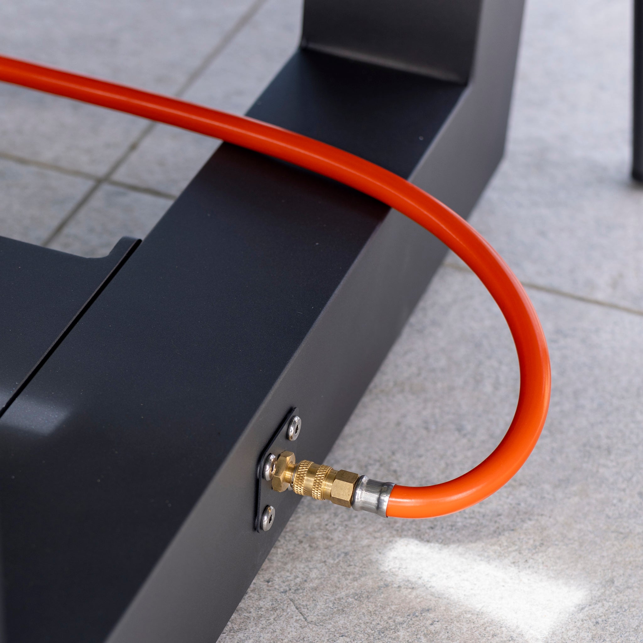 Close-up of an orange hose connected to a black device on a tiled floor, accentuating the high-quality aluminium construction throughout the Monterrey 8 Seat Rope Rectangular Ceramic Firepit Dining Set in Grey.