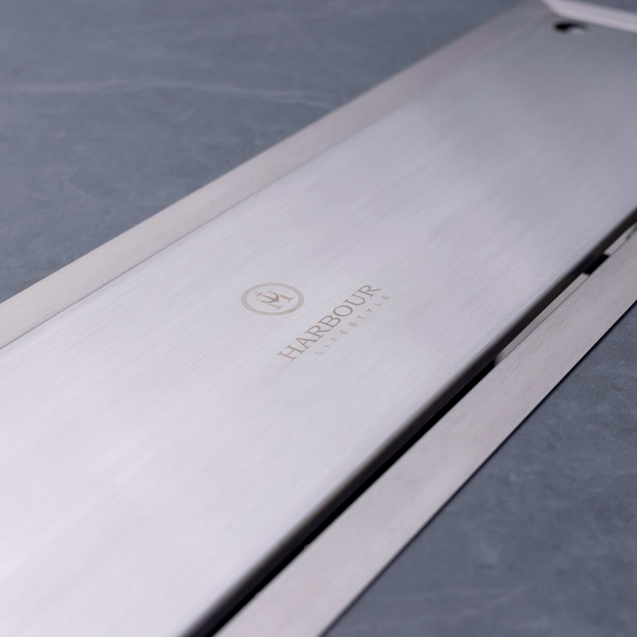 Close-up of a brushed metal surface with the logo and text "HARBOUR LIFESTYLE" etched on it, featuring our high-quality Monterrey 8 Seat Rope Rectangular Ceramic Firepit Dining Set in Grey.