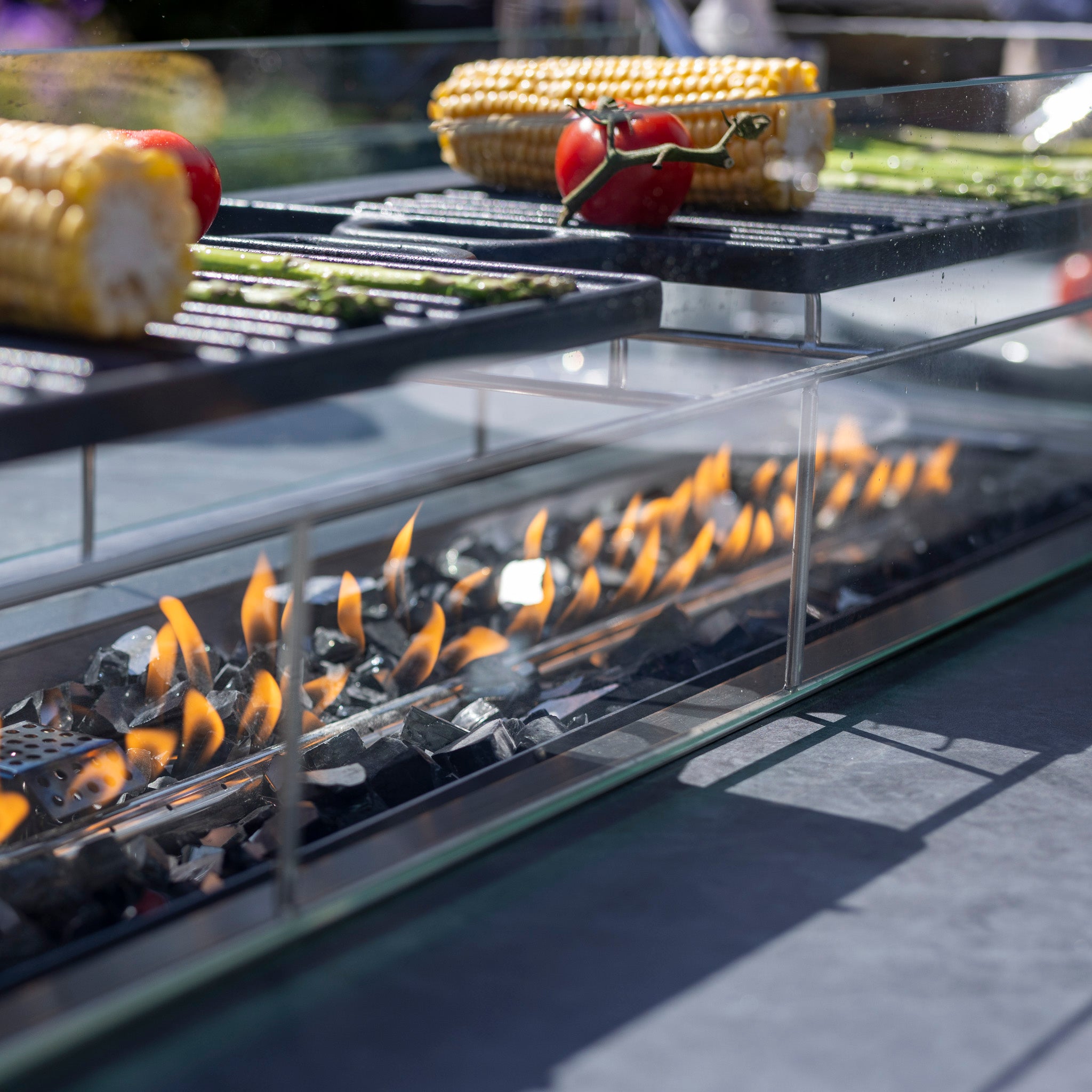 Close-up of vegetables grilling over an open flame, with corn, peppers, and asparagus on a high-quality aluminum barbecue grill from the Harbour Lifestyle Monterrey 8 Seat Rope Rectangular Ceramic Firepit Dining Set in Grey.