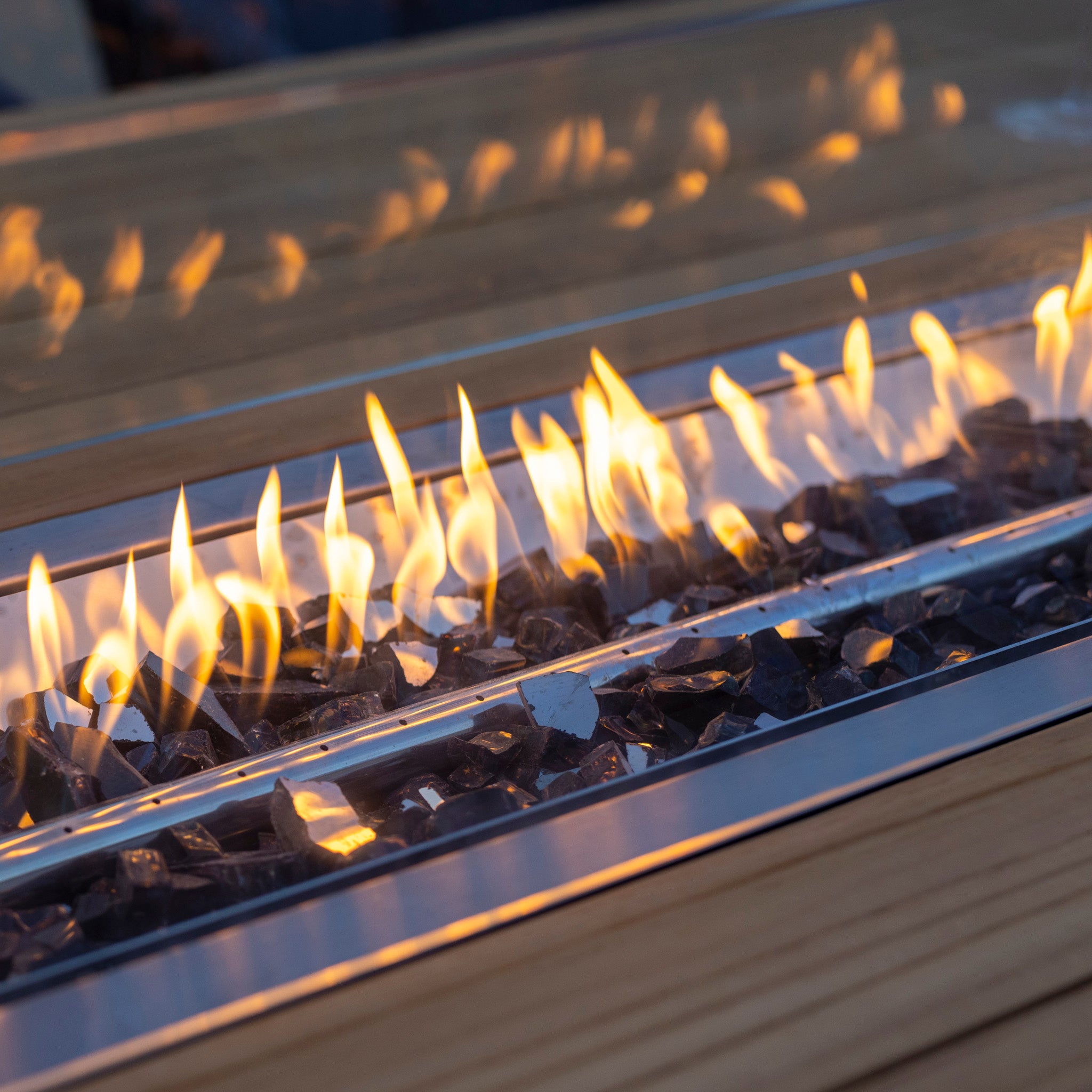 Close-up of a Monterrey 8 Seat Rope Rectangular Teak Firepit Dining Set in Grey with burning flames over black stones, seamlessly integrated into a wooden table.