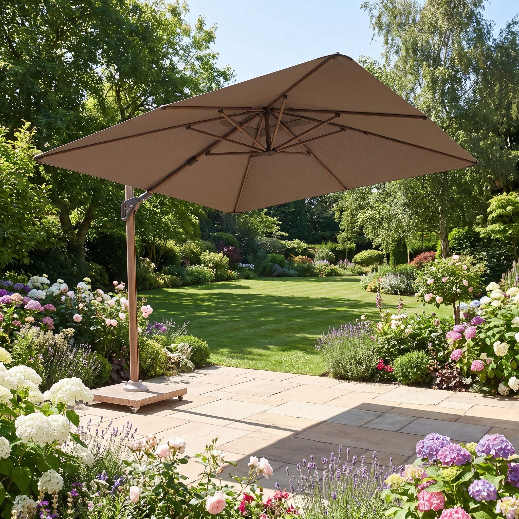 A spacious stone terrace is shaded by the Nexus T2 Premium 3m Square Cantilever Parasol in Deep Taupe with a Venezia 90kg Granite Base, complemented by contemporary garden furniture amid a colorful, lush garden on a sunny day.