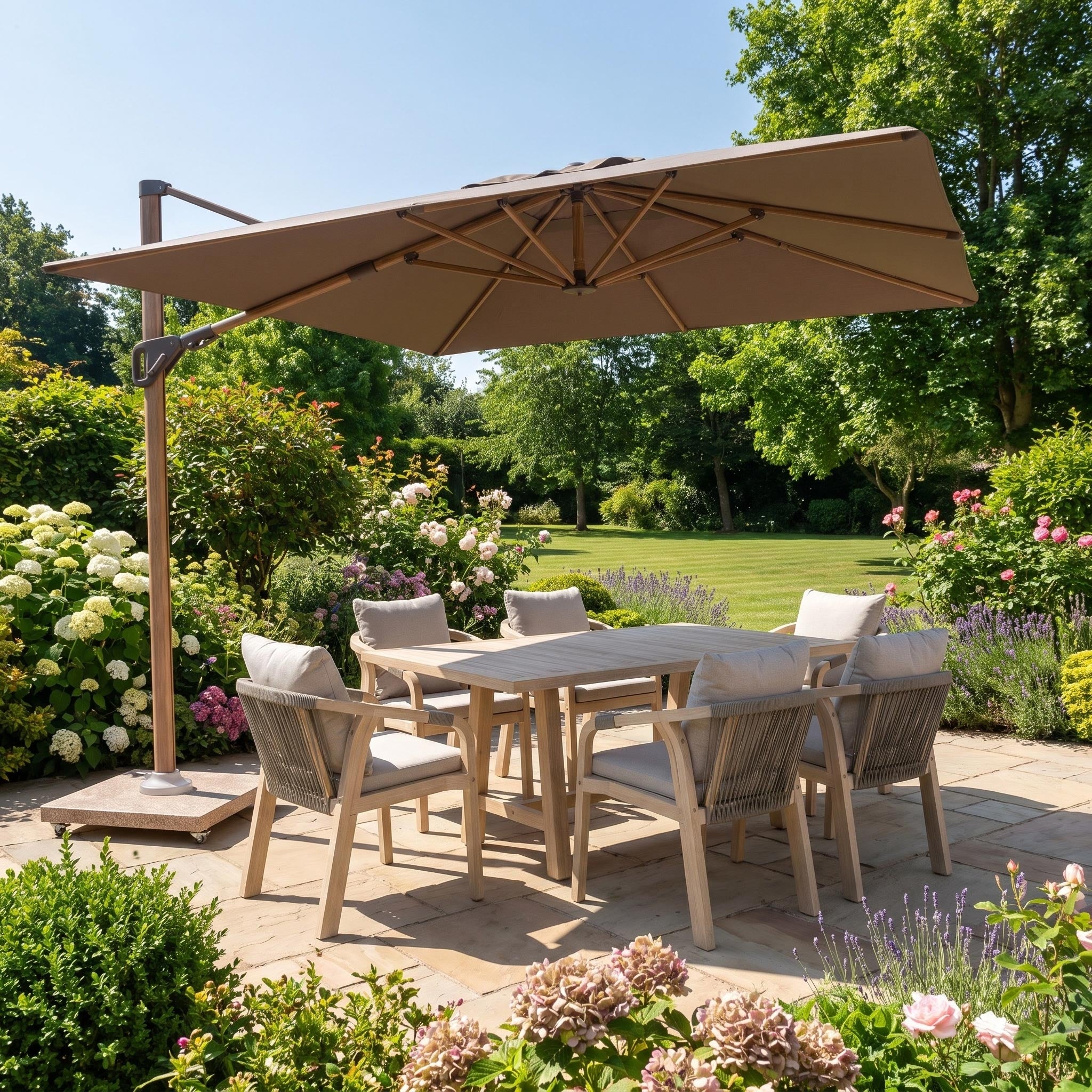 A patio set with six chairs sits under the Nexus T2 Premium 3m Square Cantilever Parasol in Deep Taupe with Venezia 90kg Granite Base, creating a stylish and contemporary outdoor space in a sunny, flower-filled garden—perfect for relaxing outdoors.
