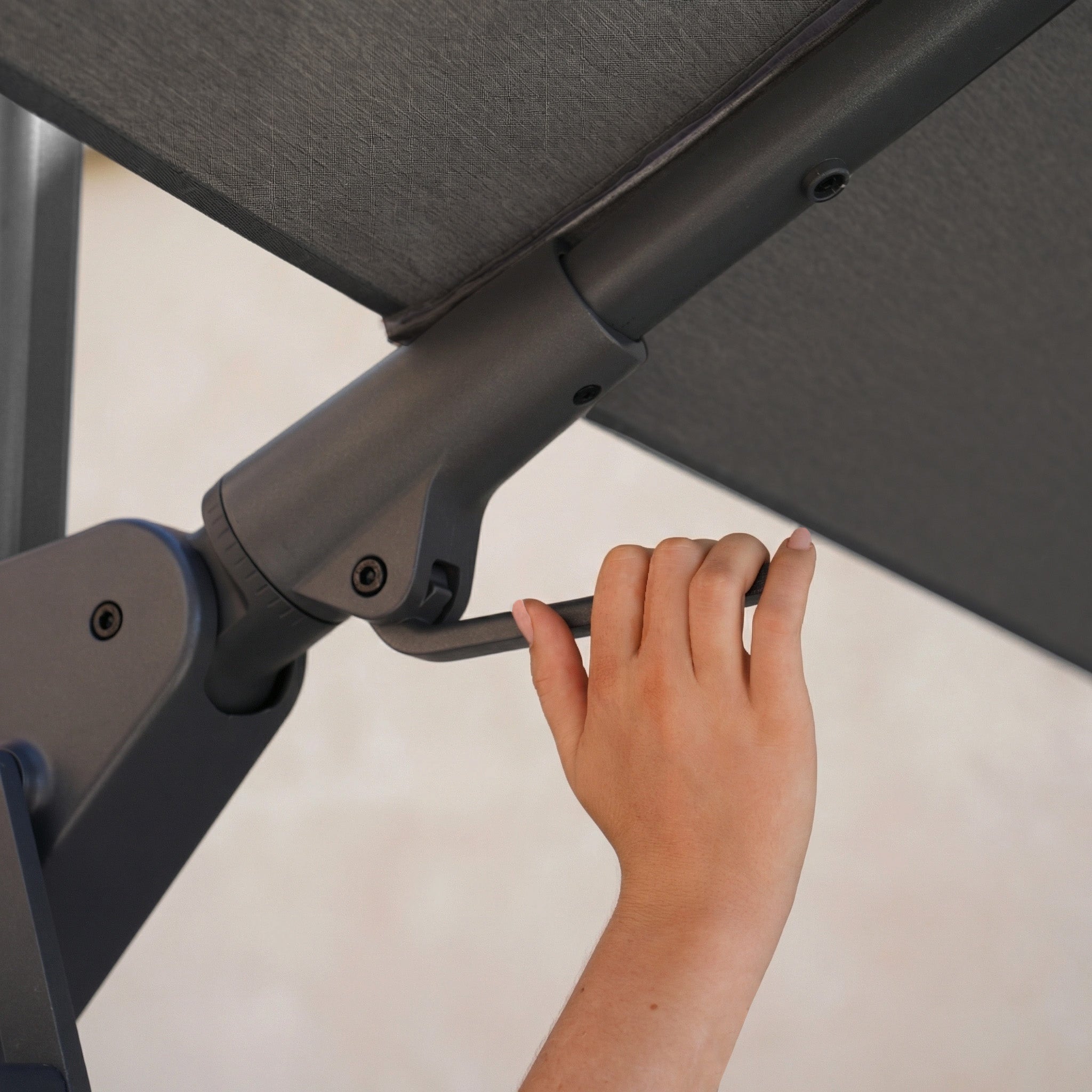 A hand turning the crank handle of the Nexus T2 Premium 3m Square Cantilever Parasol in Black with 90kg Granite Base, designed for smooth 360-degree rotation in any outdoor space.