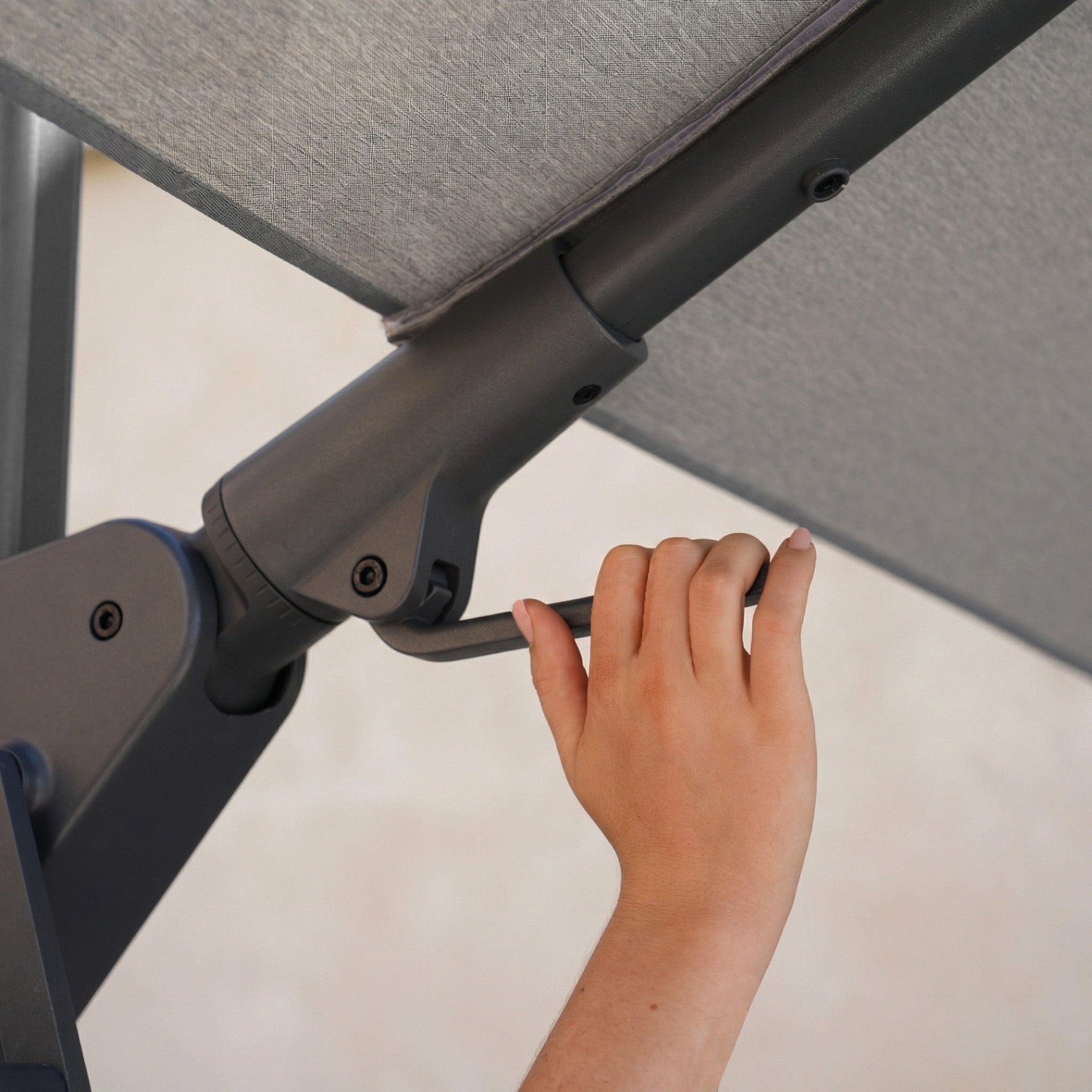 A hand turns the crank handle to adjust the Nexus T2 Premium 3m Square Cantilever Parasol in Manhattan Grey with 90kg Granite Base, enabling smooth 360-degree rotation for optimal shade.