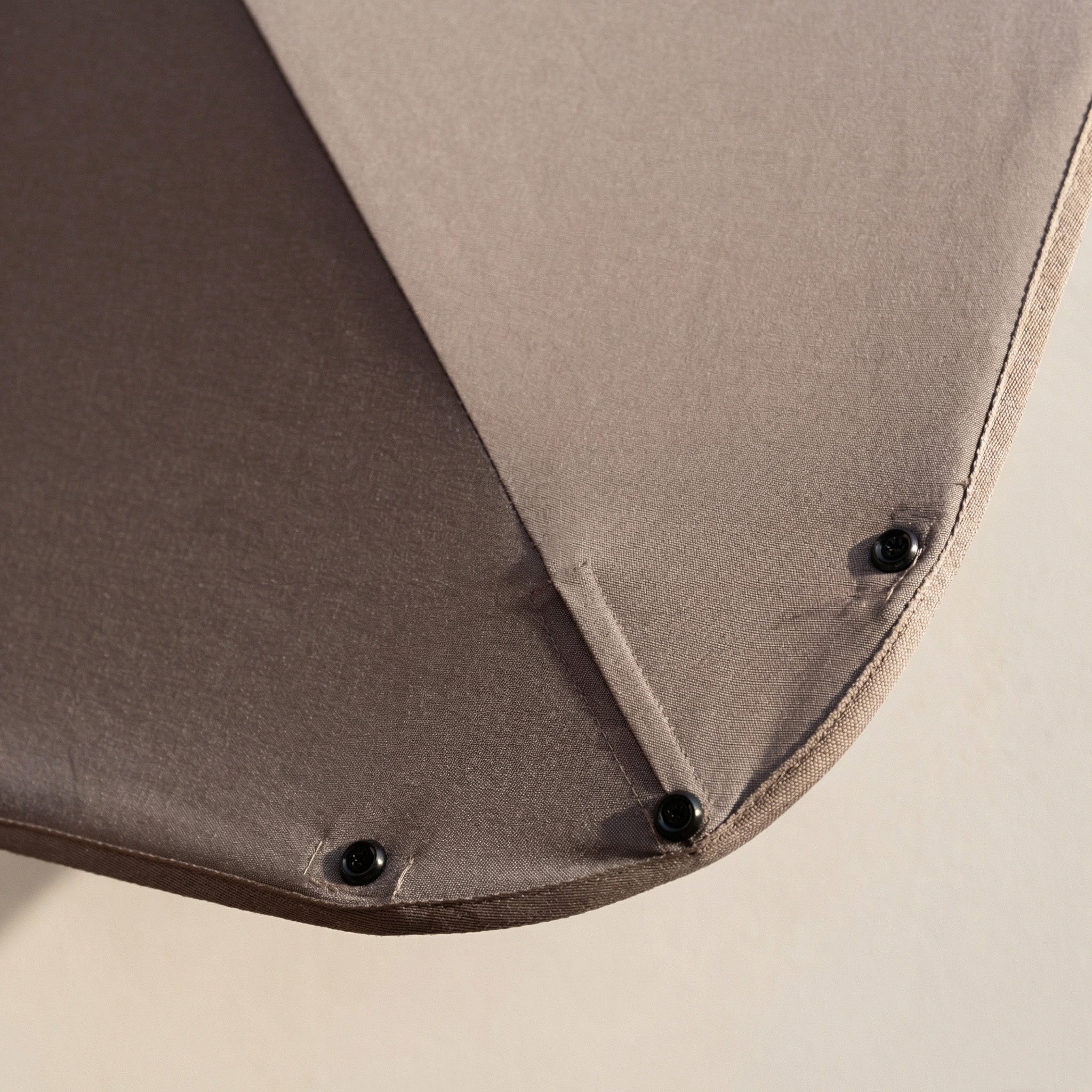 Close-up of a beige fabric corner with three black buttons, part of a garden furniture set—ideal to pair with the Nexus T2 Premium 3m Square Cantilever Parasol in Deep Taupe with 90kg Granite Base on your patio.