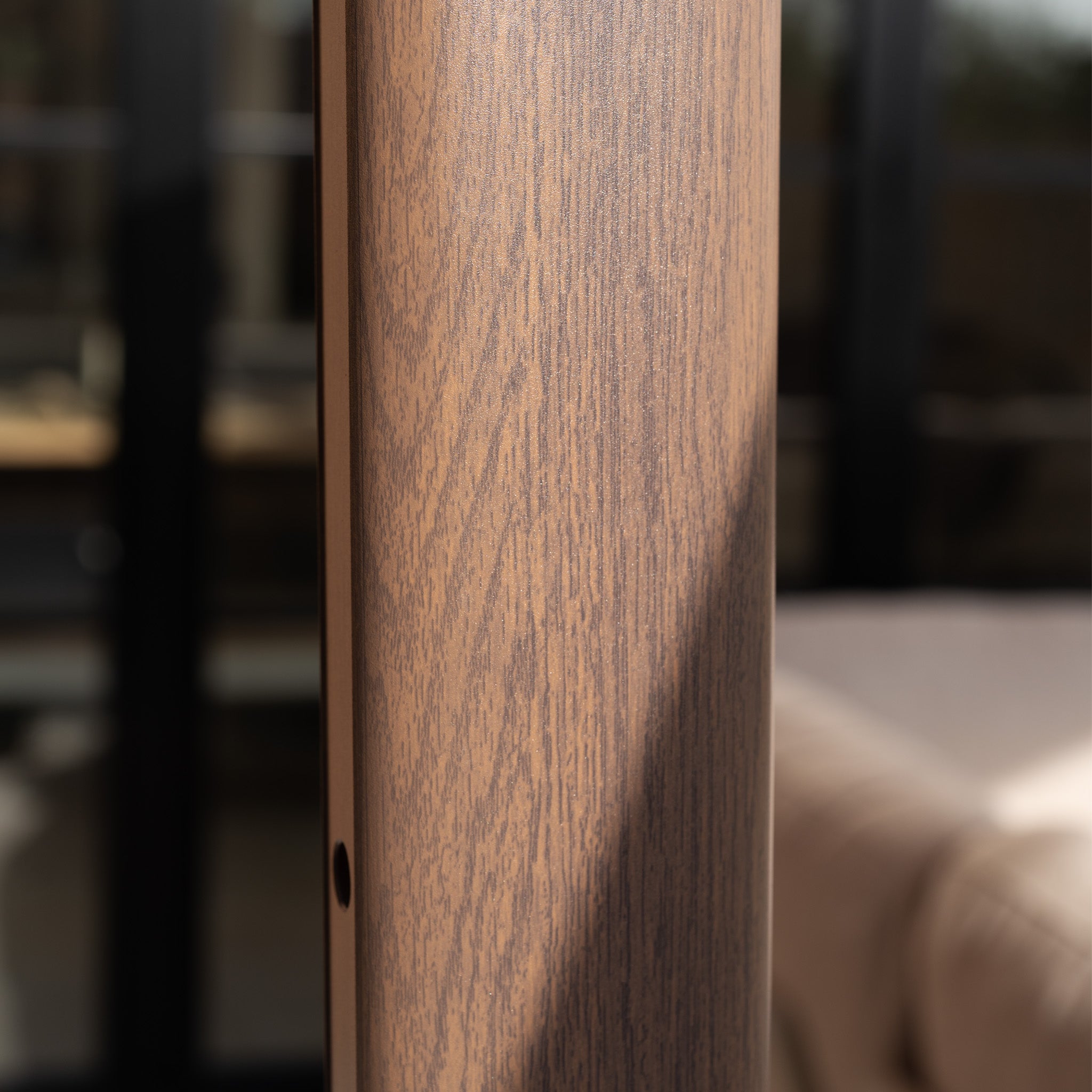 Close-up of vertical wooden grain with blurred outdoor furniture and glass in the background, hinting at a Nexus T2 Premium 3m Square Cantilever Parasol in Deep Taupe with 90kg Granite Base.