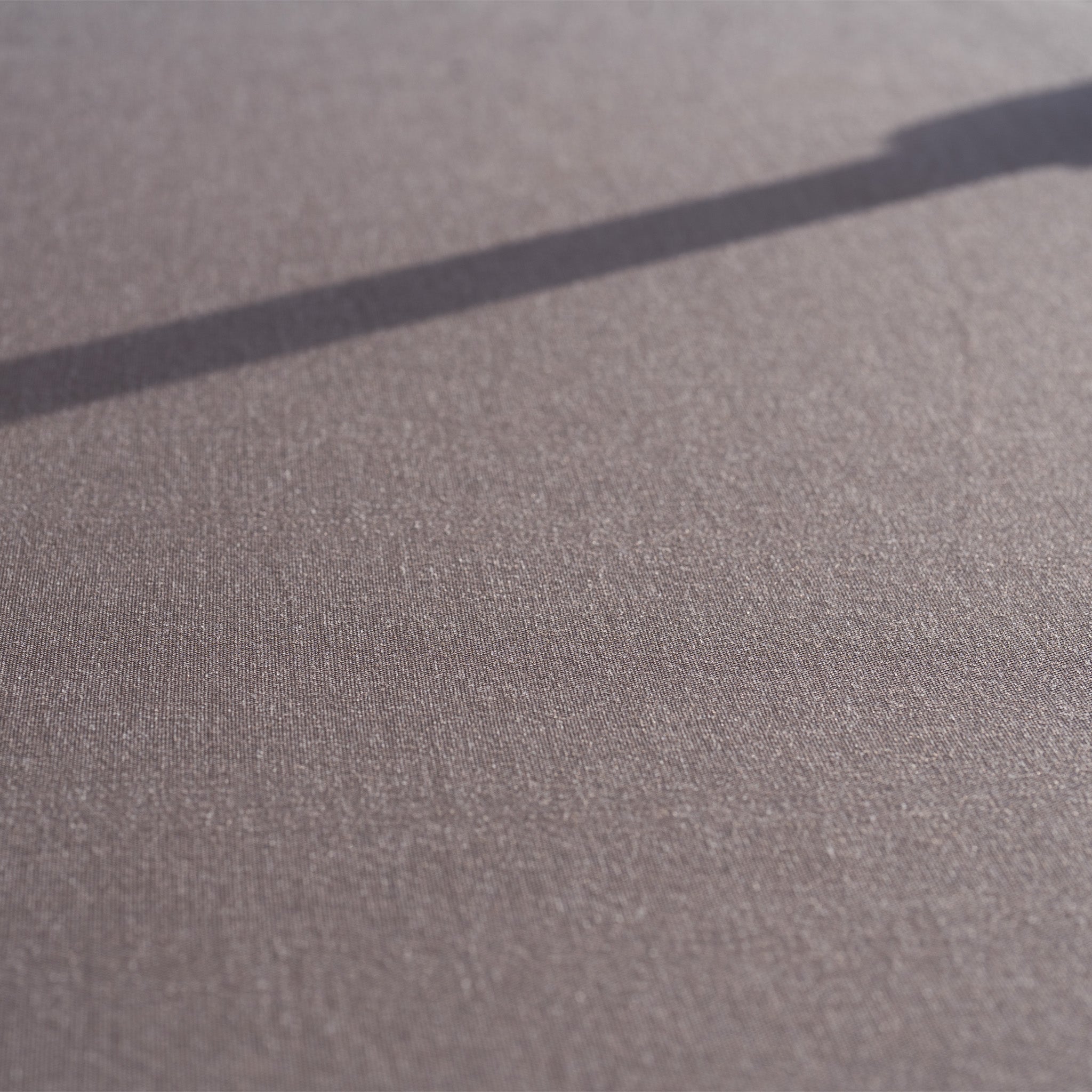 A textured brown surface with a dark diagonal shadow—likely cast by the Nexus T2 Premium 3m Square Cantilever Parasol in Deep Taupe with 90kg Granite Base—crosses the upper right corner.