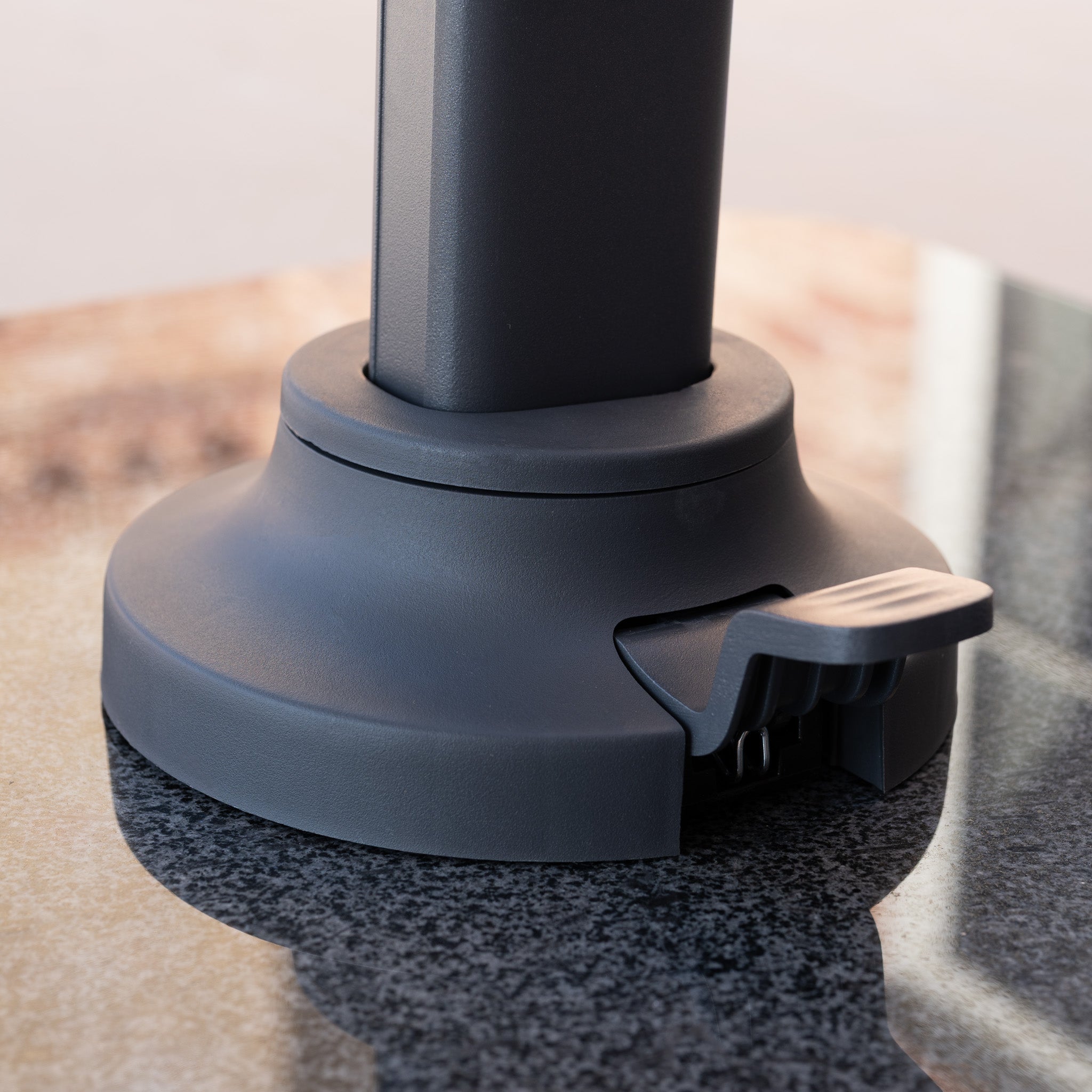 Close-up of the Nexus T2 Premium 3m Square Cantilever Parasol in Manhattan Grey, featuring a 90kg granite base and locking lever on a reflective surface.
