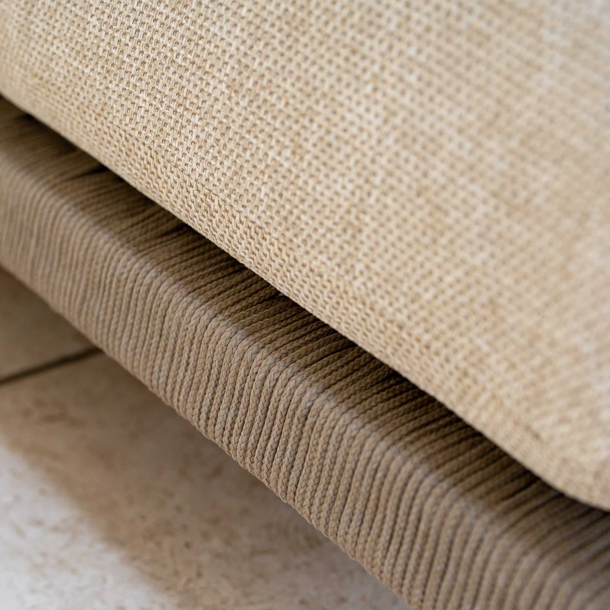 Close-up of beige textured cushions stacked on corduroy, with tiled floor below—perfect accents for the Noah Corner Sofa Set with Armchair in Volga Grey or rustic teak outdoor furniture.