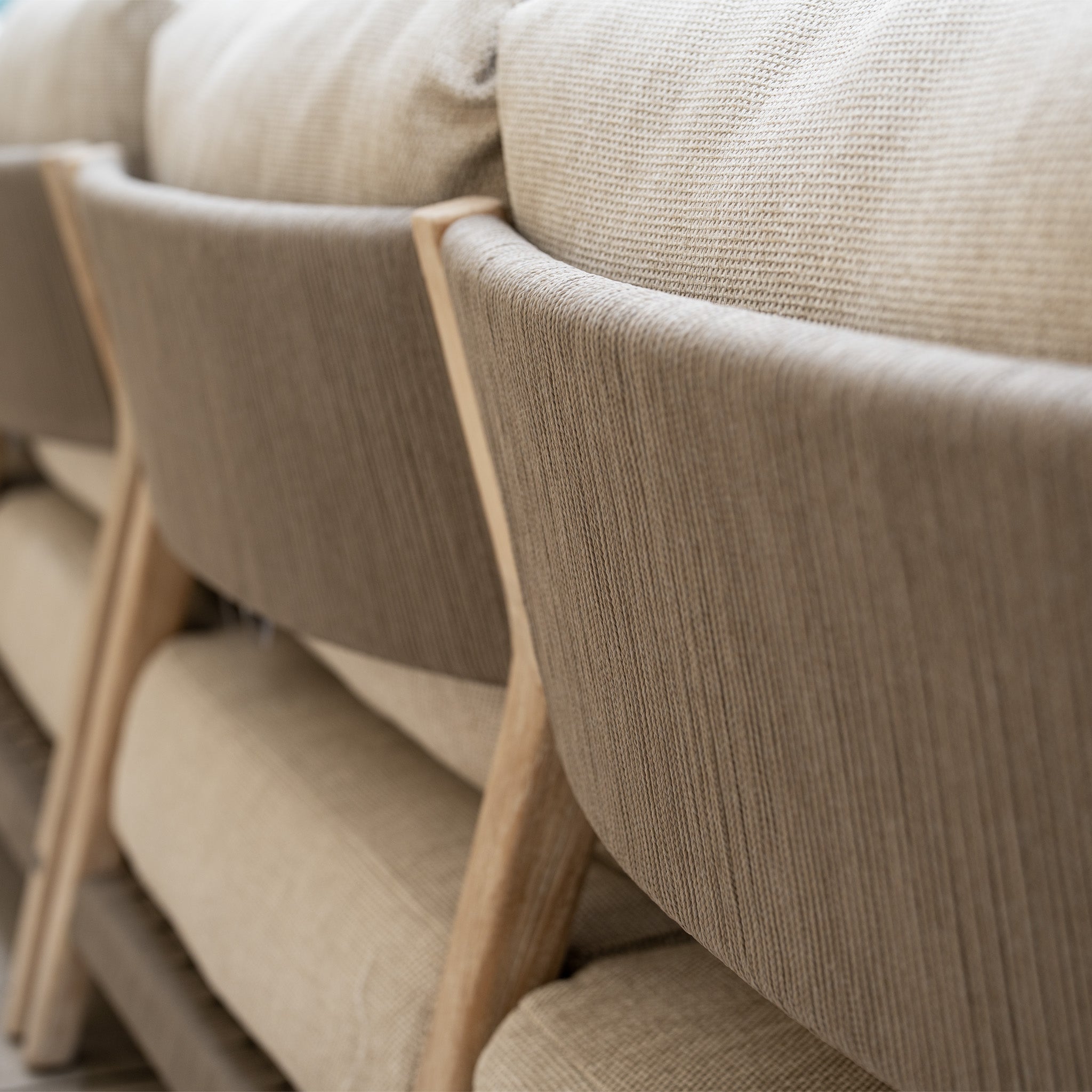 Close-up of beige upholstered chairs lined up behind a matching textured fabric sofa from the Noah Corner Sofa Set with Armchair in Volga Grey.