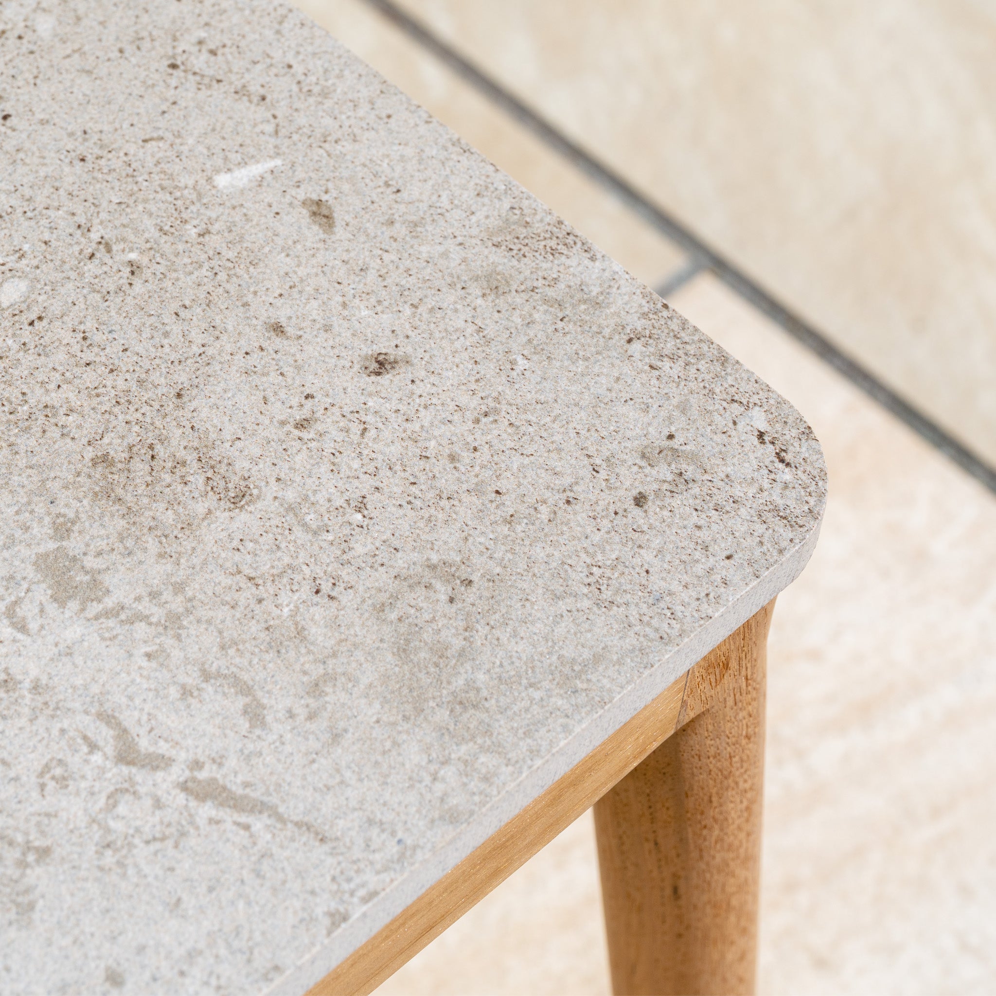 Close-up of a light beige, stone-textured tabletop with wooden legs on a tiled floor, perfectly complementing your weather-resistant furniture or the New York 3 Seat Sofa Set for a stylish outdoor arrangement.